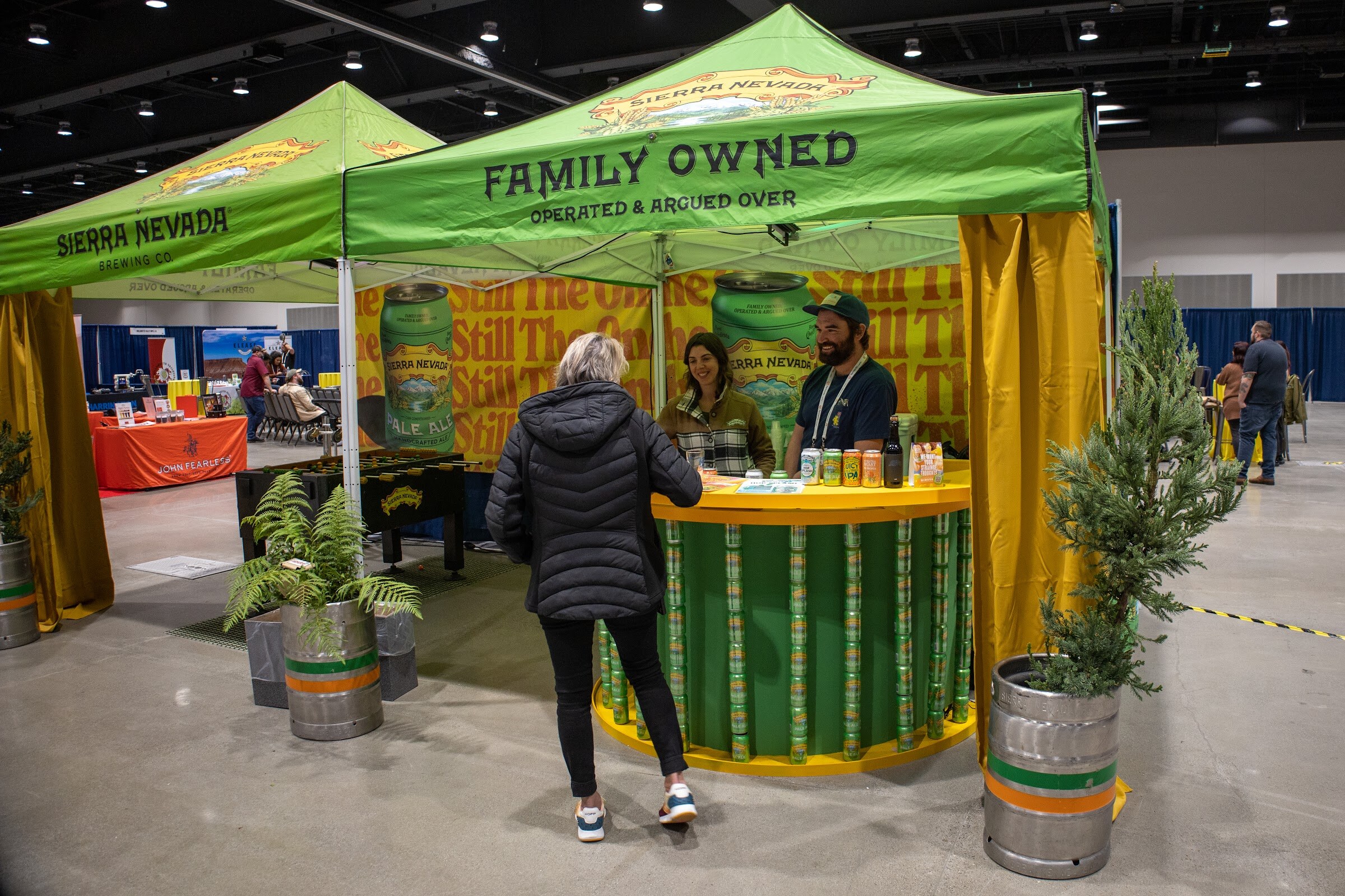 Green tents with a Family Owned sign and Sierra Nevada branding over a bar of cans, with a person in a black jacket standing at the counter