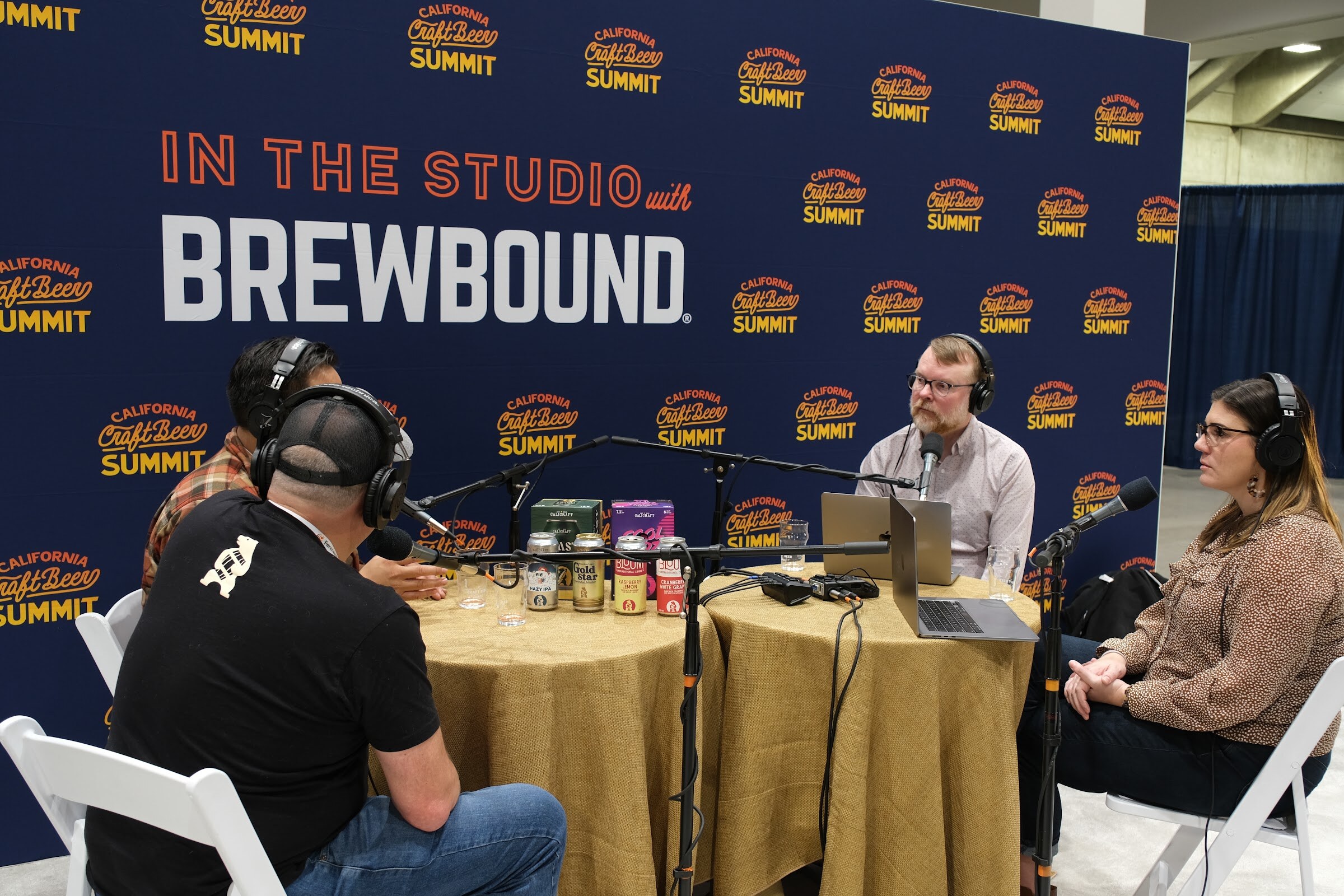 A wide view of a podcast recording at a round table in front of a navy In the Studio with Brewbound and California Craft Beer Summit backdrop