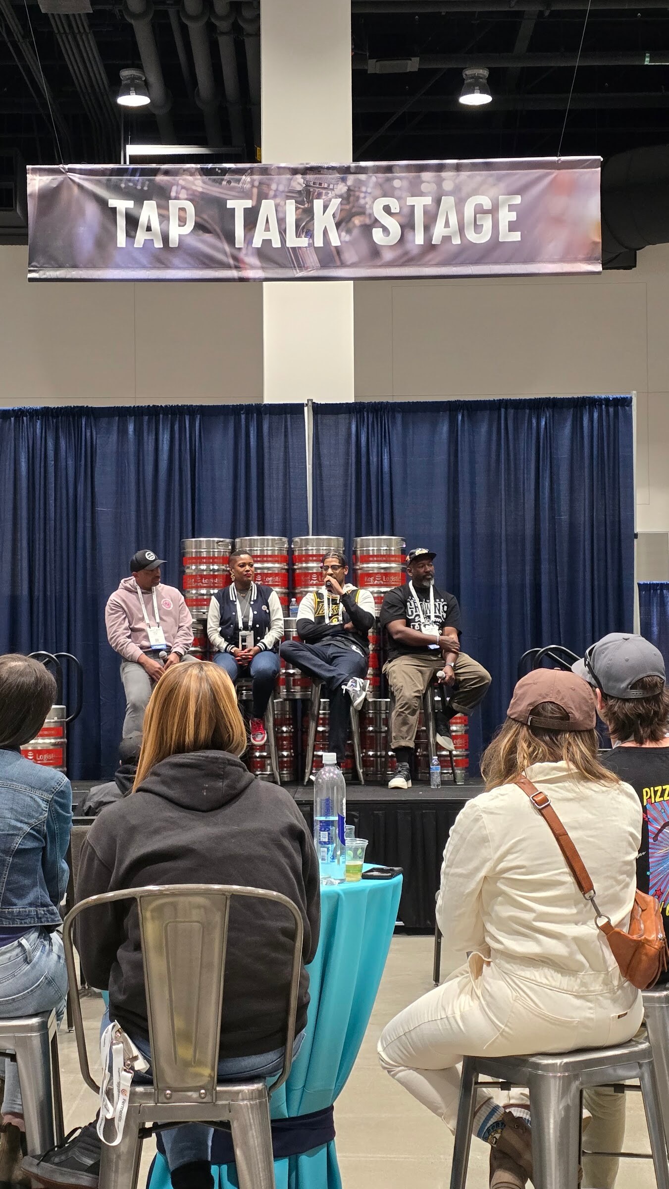 A small panel seated on a stage under a Tap Talk Stage banner with an audience of attendees in front