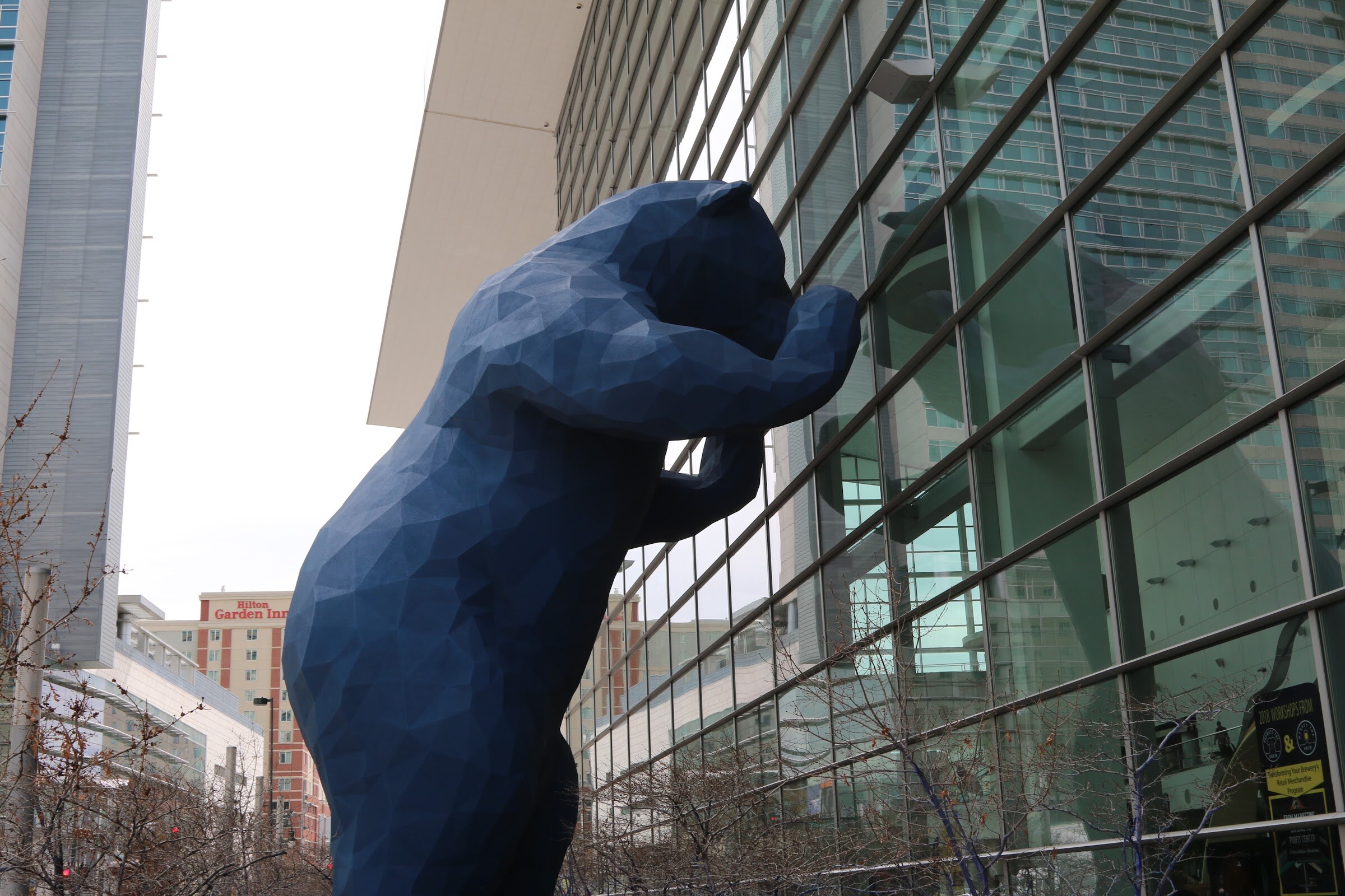 A large blue faceted bear sculpture leaning against the glass facade of the convention center.