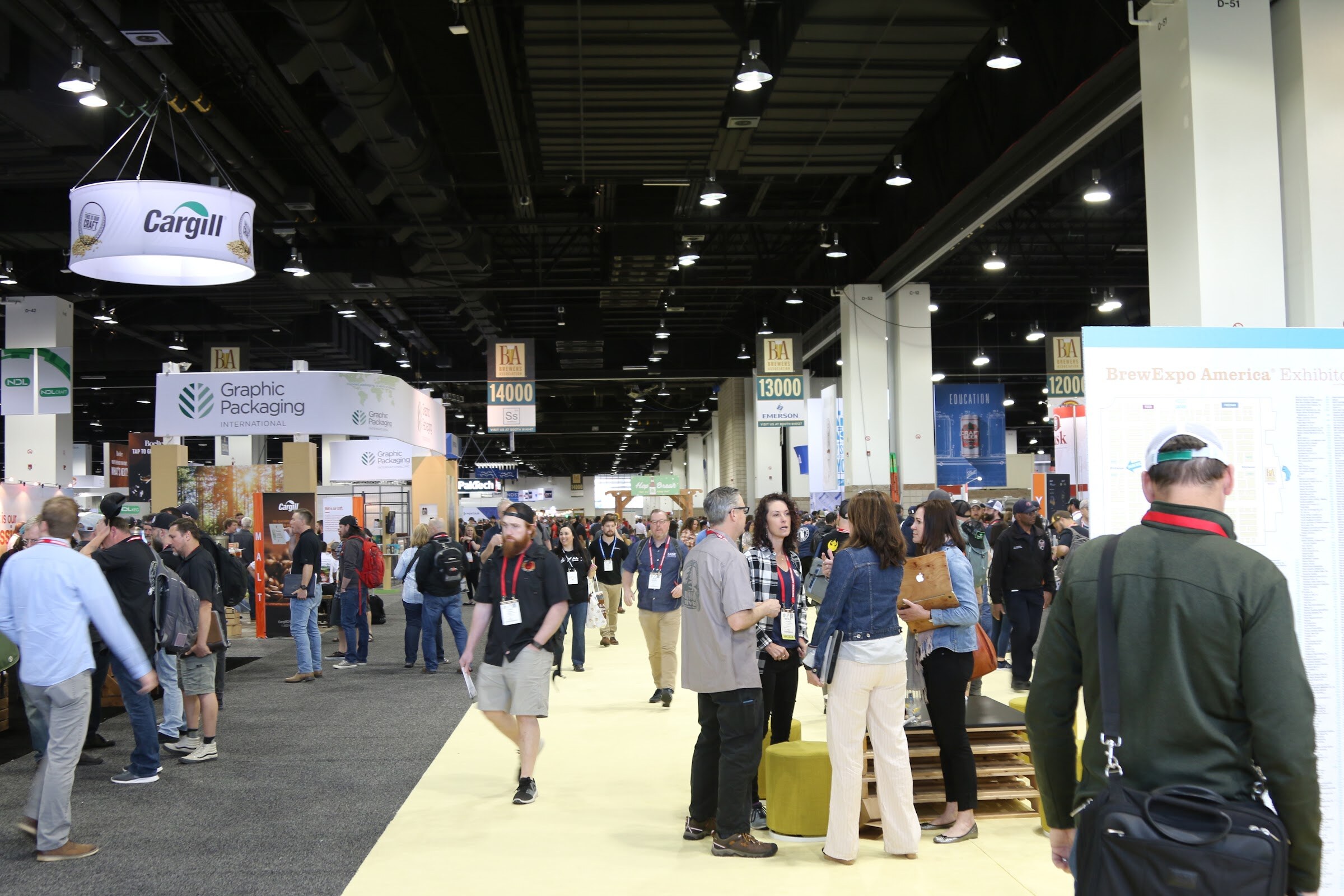 Crowd walking along an aisle of exhibitor booths under a hanging Cargill sign inside the convention hall.