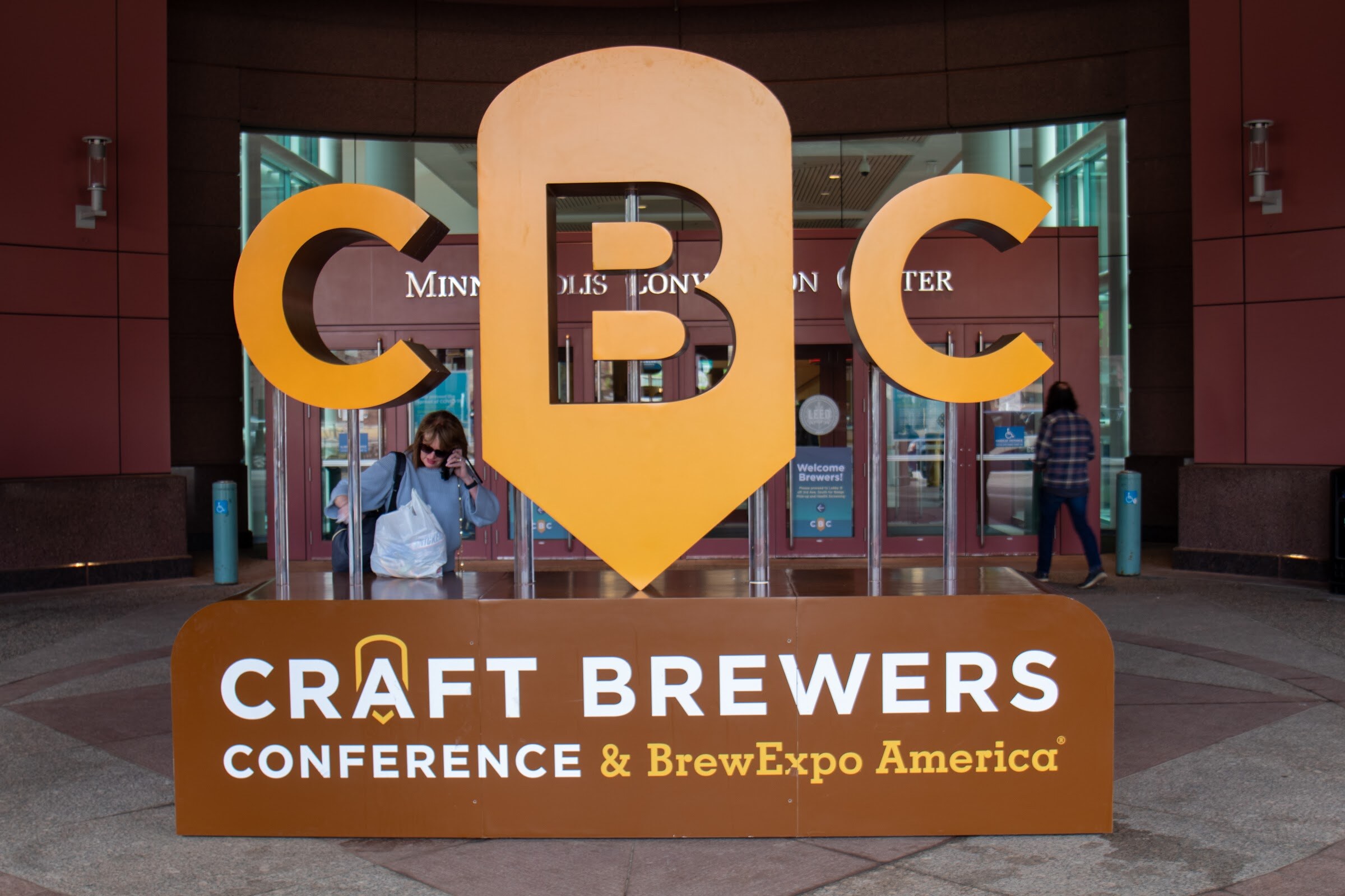 A large orange and brown CBC sign reading Craft Brewers Conference and BrewExpo America stands in front of the Minneapolis Convention Center entrance