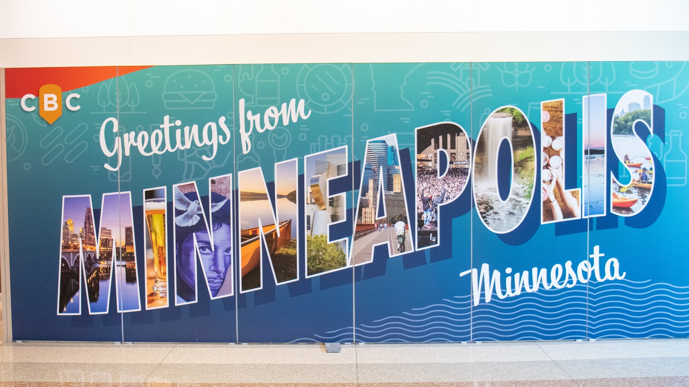 A blue and teal postcard-style CBC mural reads Greetings from Minneapolis, Minnesota in a hallway