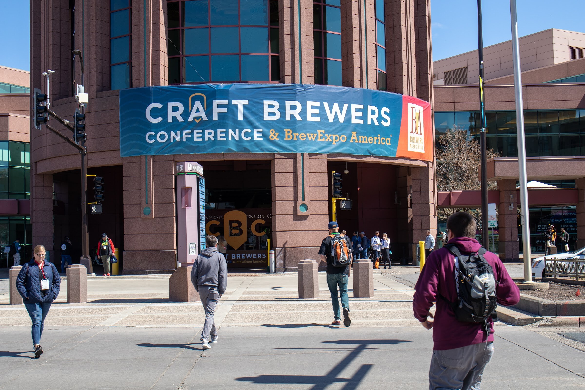 Attendees cross the street toward the convention center entrance under a blue Craft Brewers Conference and BrewExpo America banner