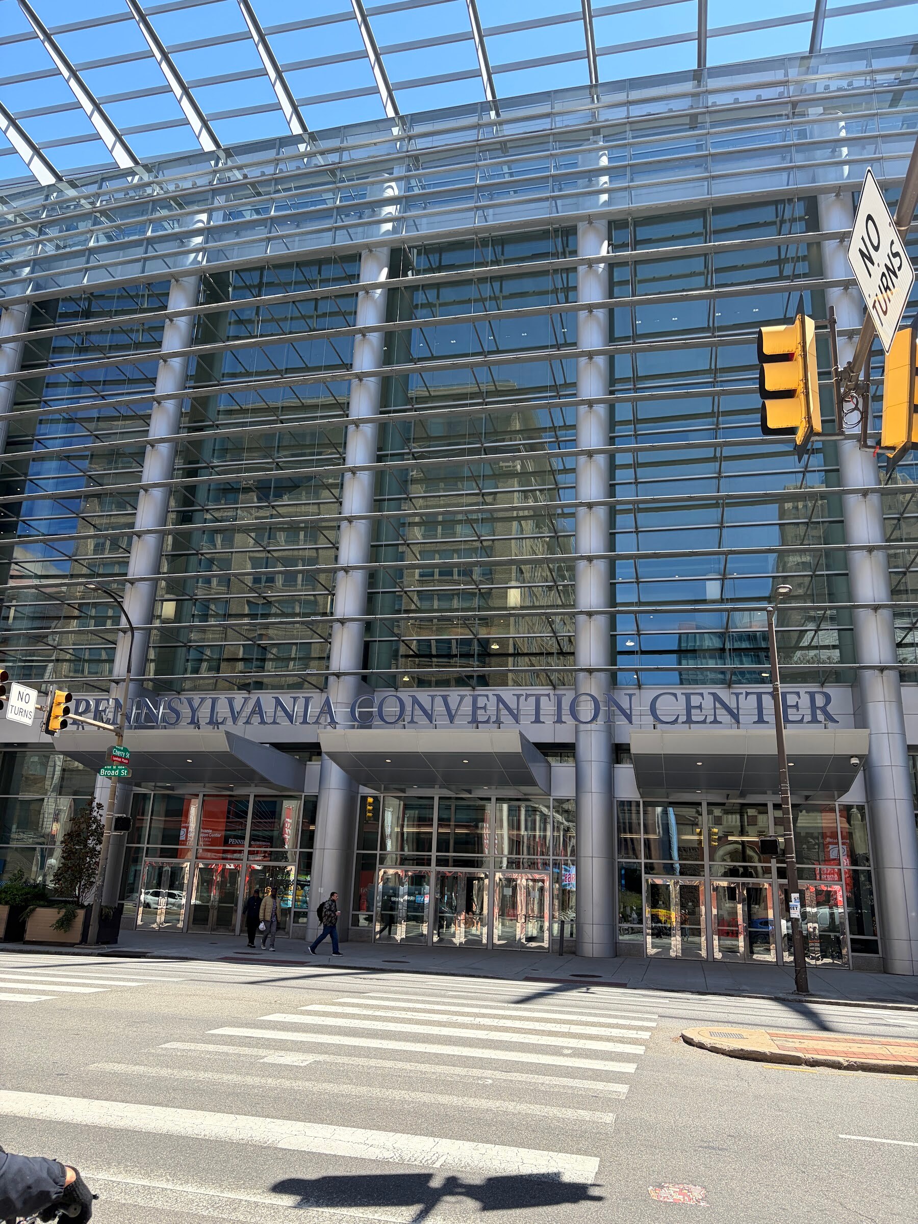 Glass facade of the Pennsylvania Convention Center under a clear blue sky, with a crosswalk in the foreground.