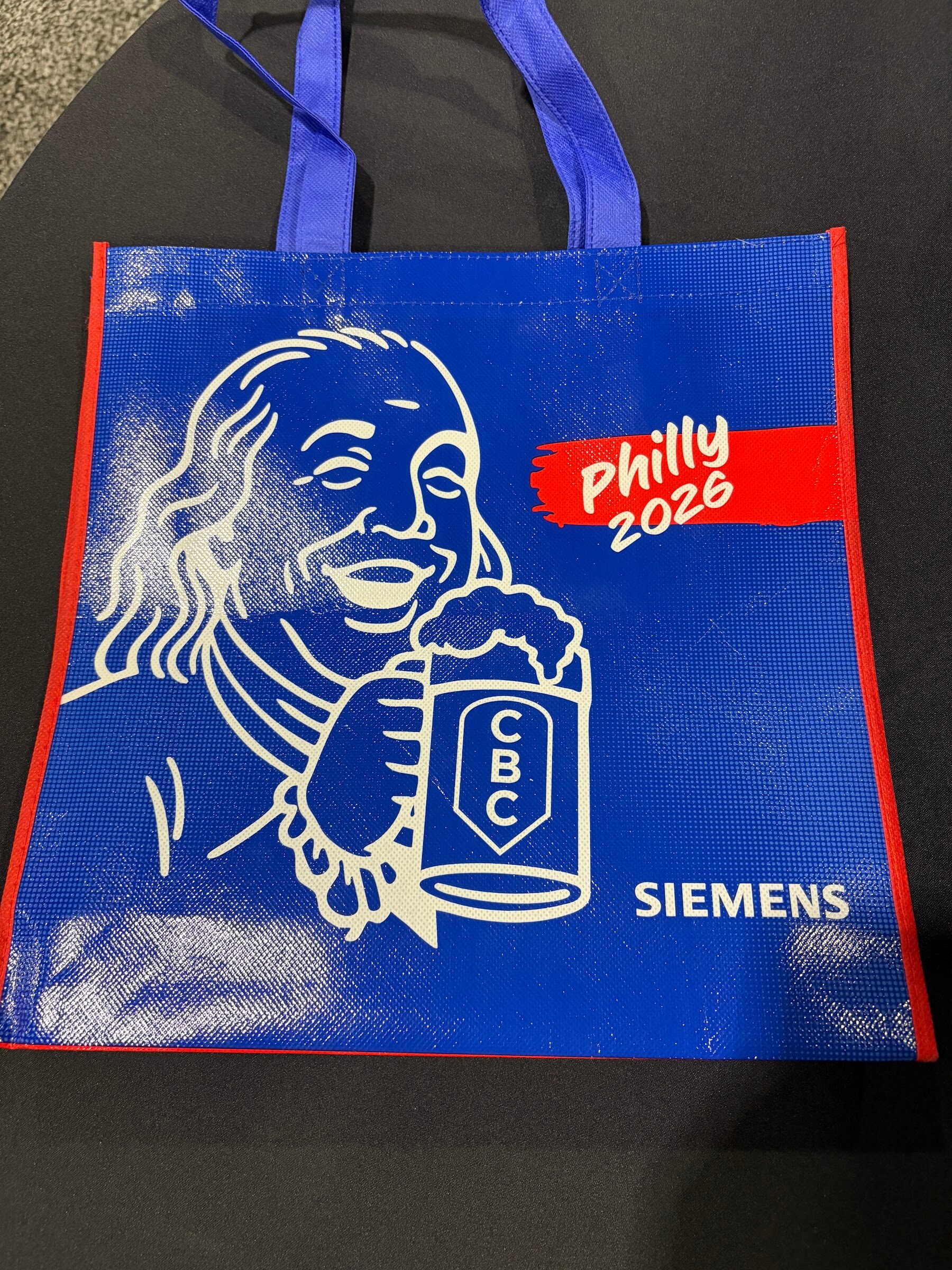 Blue tote bag printed with a Benjamin Franklin illustration holding a CBC beer and the words Philly 2026 and Siemens.