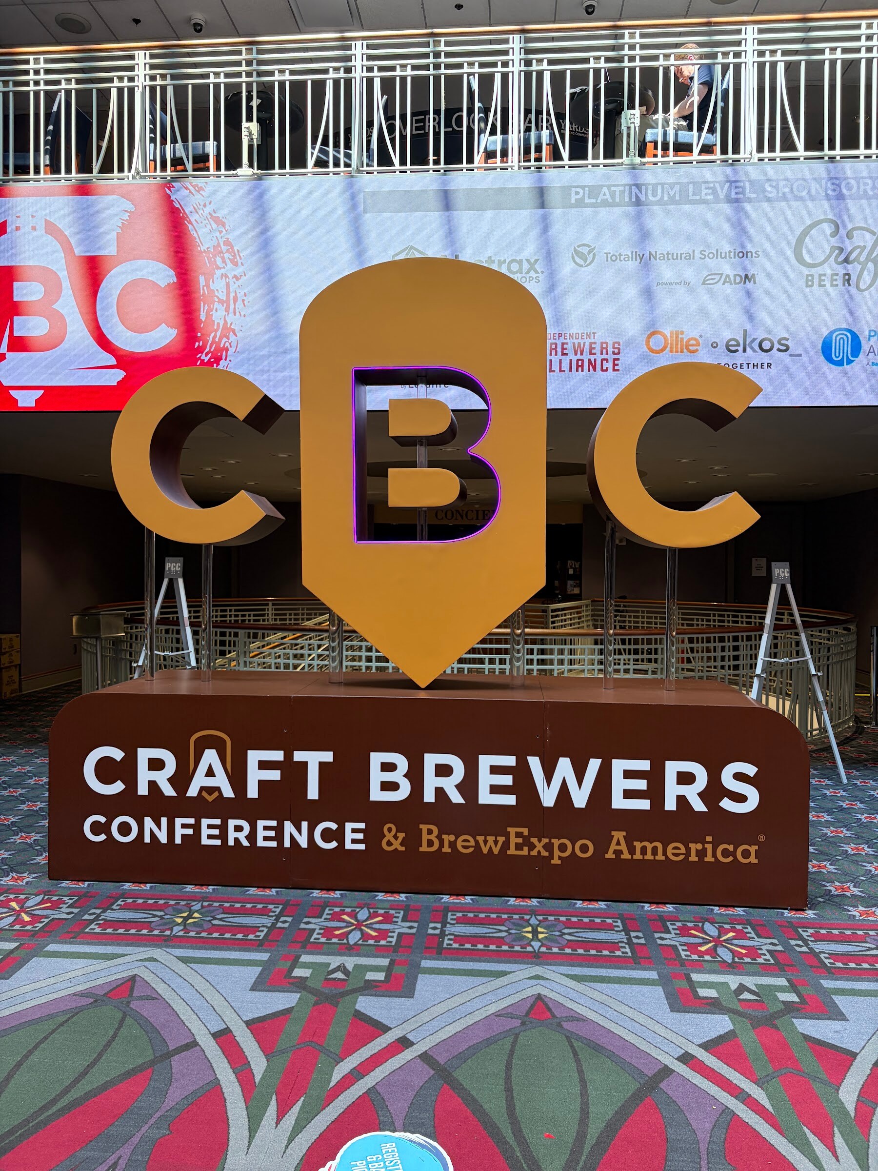 Large freestanding CBC letters above a sign reading Craft Brewers Conference & BrewExpo America on a patterned carpet.
