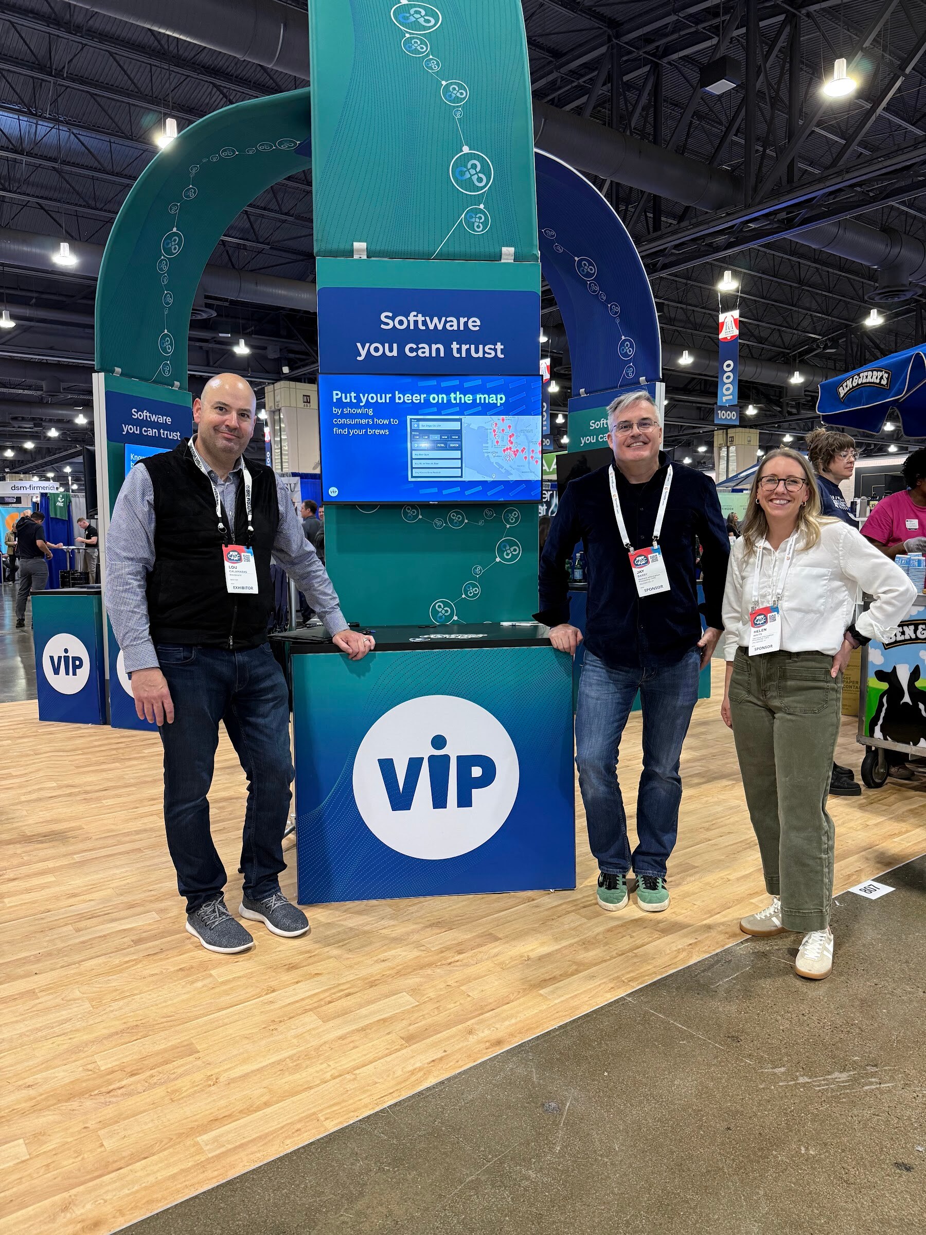 Three people stand beside a teal VIP booth with a screen reading Software you can trust.