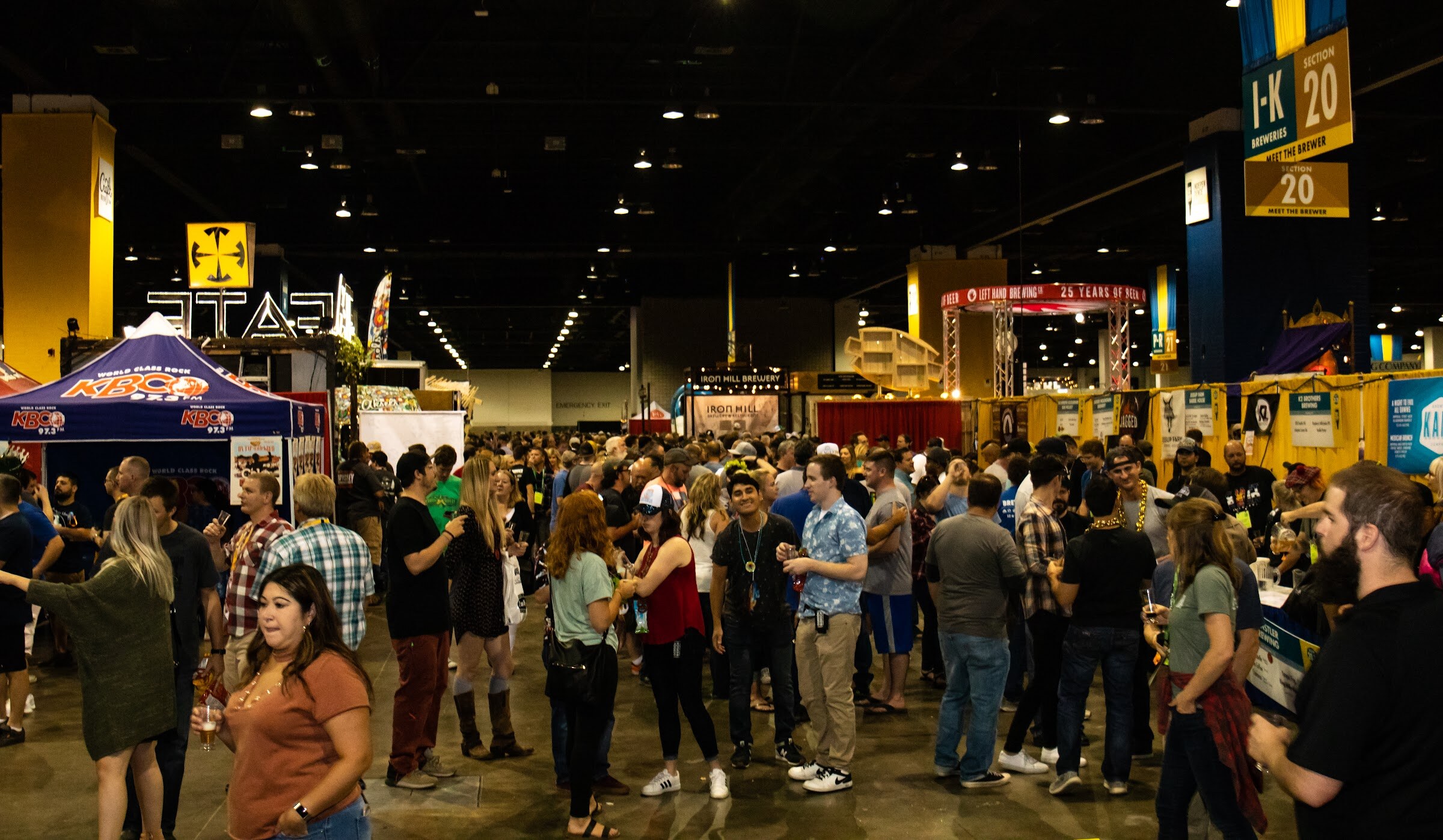 A busy convention hall with hundreds of attendees, brewery booths, a KBCO tent, an Iron Hill Brewery sign and a hanging section 20 sign.