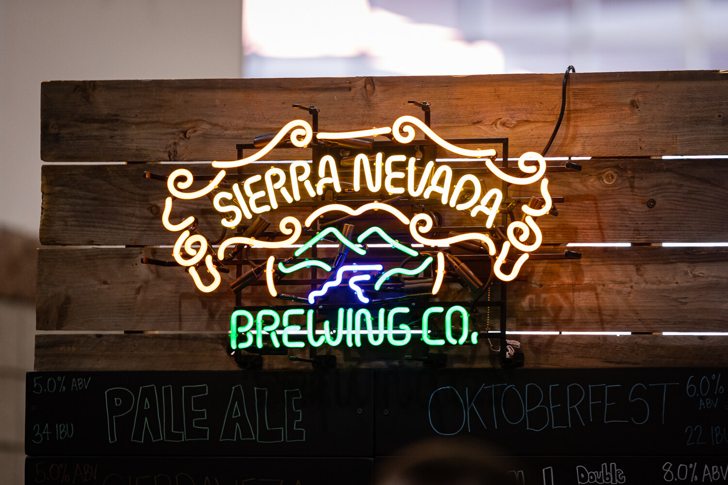 A neon Sierra Nevada Brewing Co. sign on a wooden board above a chalkboard listing Pale Ale and Oktoberfest.
