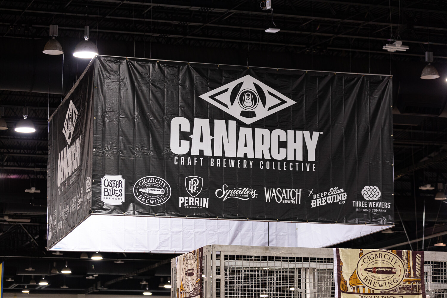 A black hanging booth sign reading CANarchy Craft Brewery Collective with the logos of its member breweries below.