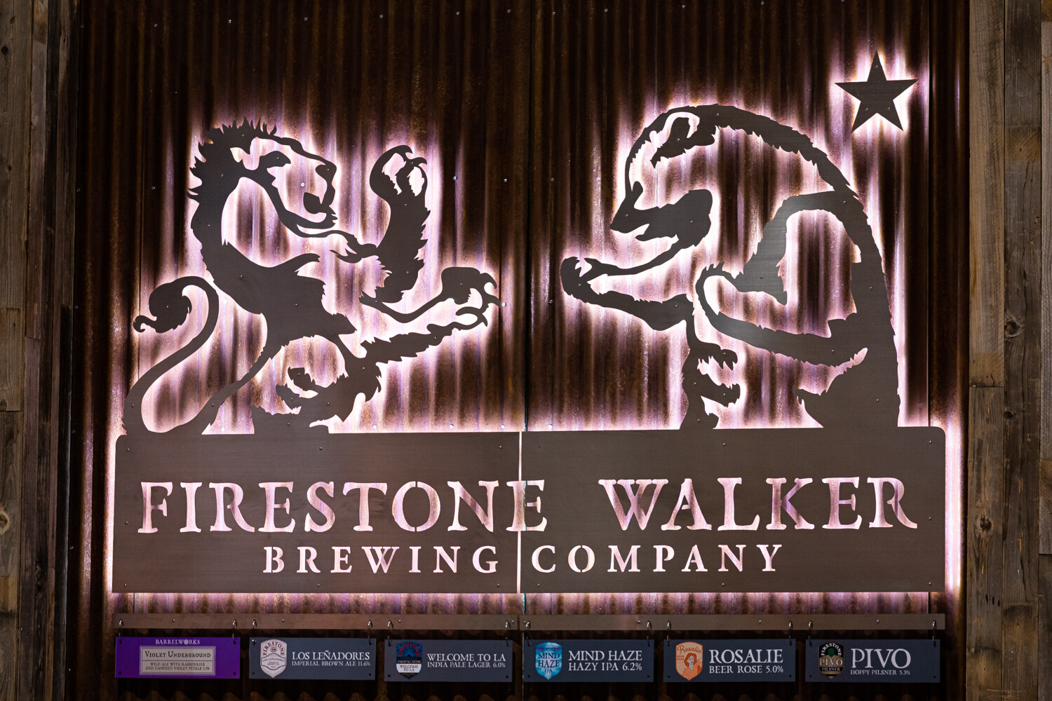 A backlit metal sign of two lions and the words Firestone Walker Brewing Company over a row of small beer labels.
