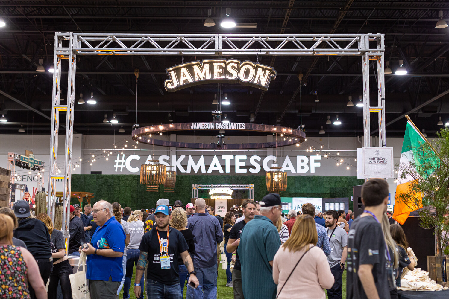 A metal truss with a lit Jameson sign above a #CaskmatesGABF wall, with attendees walking below.
