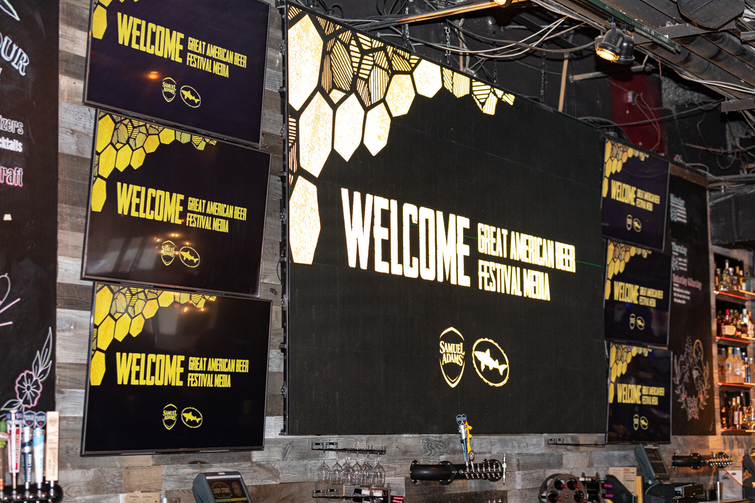 A wall of screens reading Welcome Great American Beer Festival Media with gold honeycomb graphics and Samuel Adams and Dogfish Head logos.