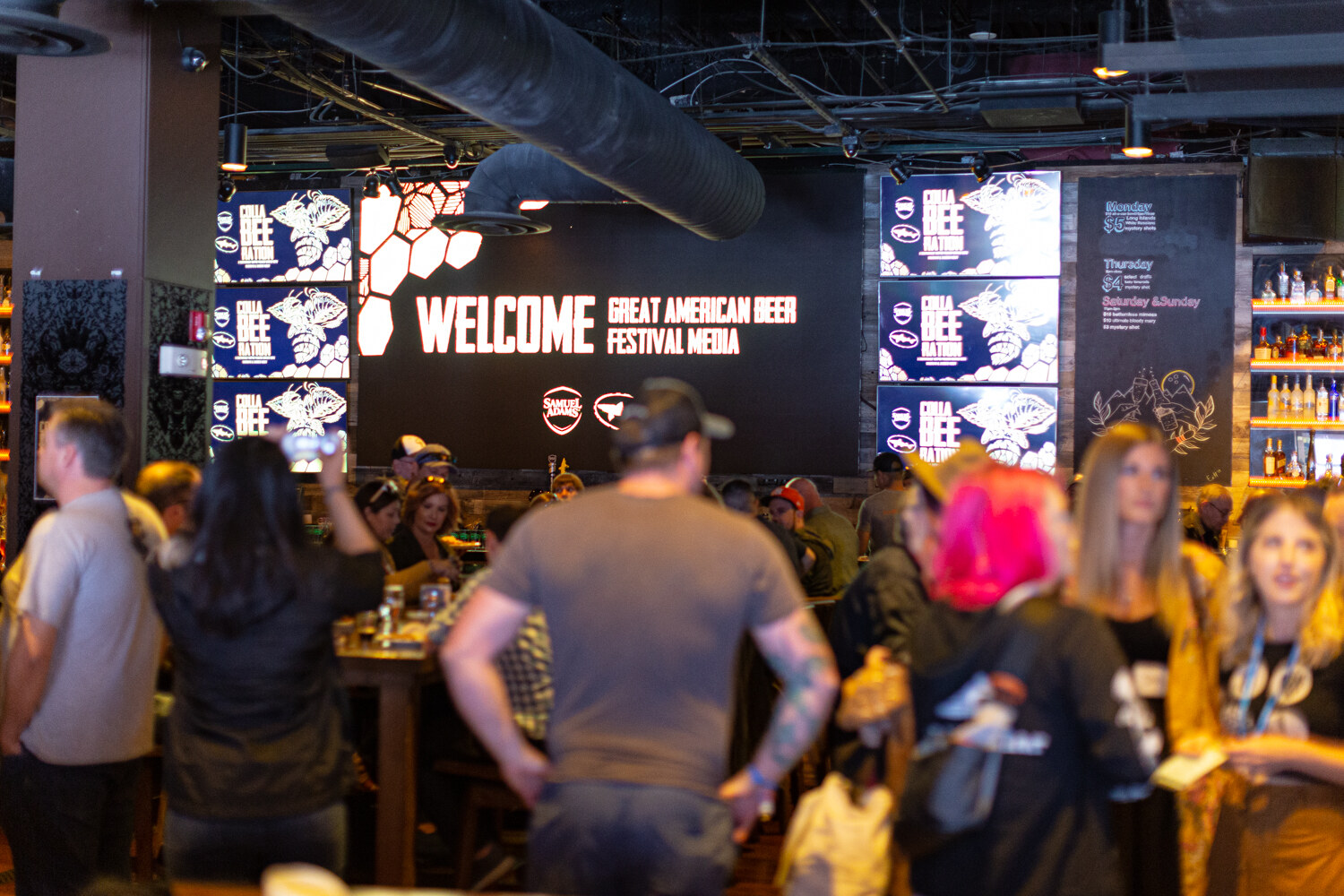 A crowded bar with a large screen reading Welcome Great American Beer Festival Media, guests in the foreground.