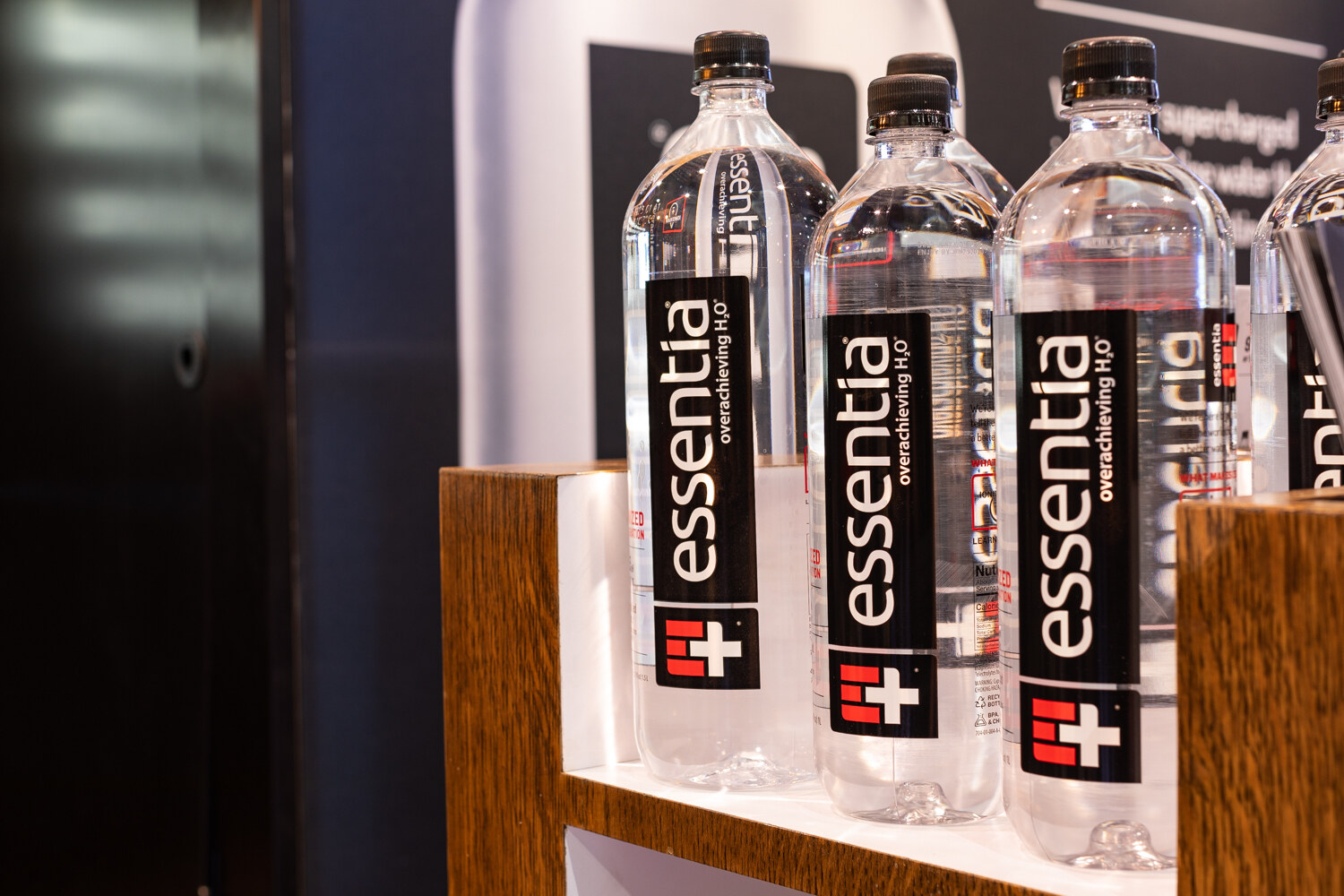 Three tall black-labelled Essentia water bottles on a white shelf.