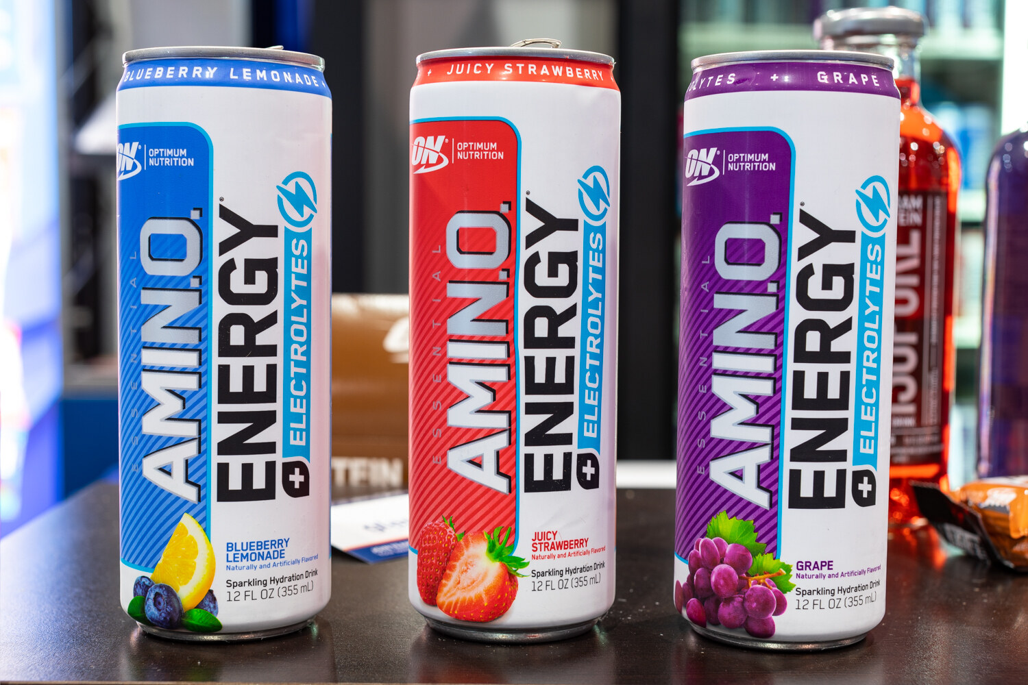 Three tall Amino Energy cans on a dark table.