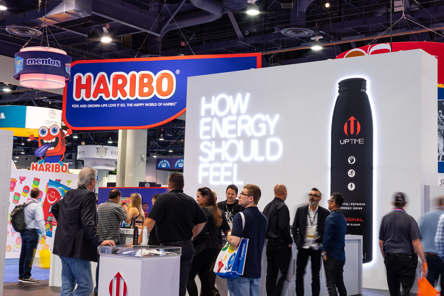 A group of attendees with badges in front of a large white Haribo booth wall showing an Uptime bottle.