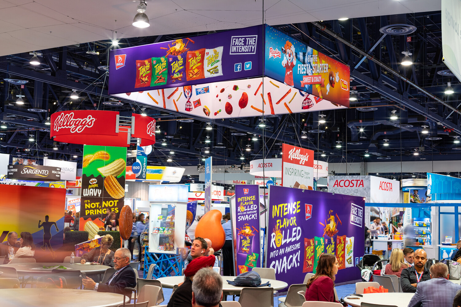 A large hall with colorful hanging banners for Kellogg's and Acosta and attendees seated at tables.