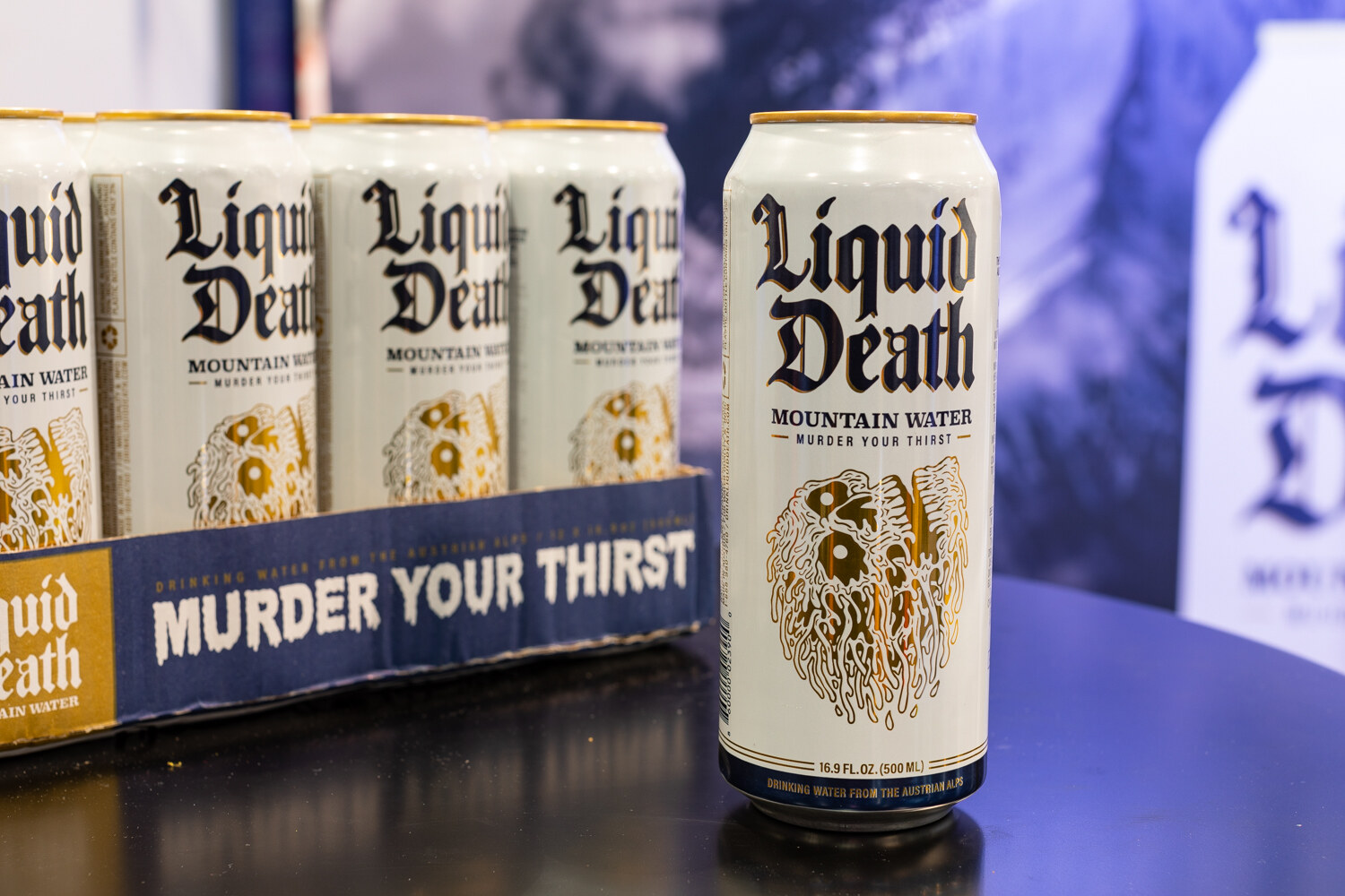 A Liquid Death can in front of a cardboard case of cans on a table.