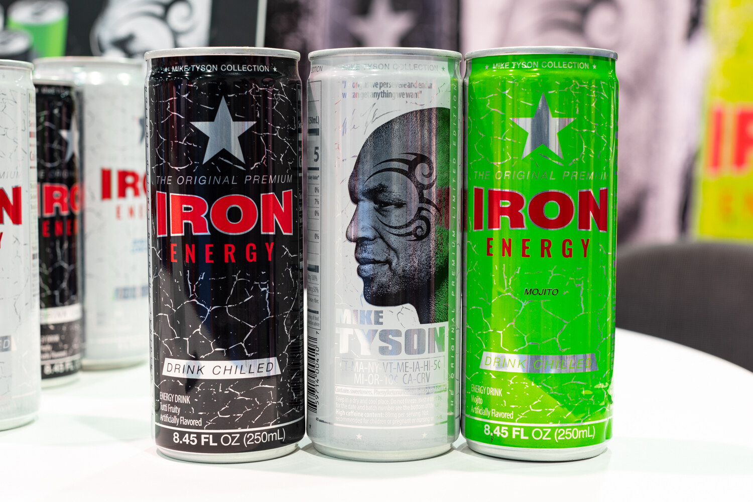 Three Iron Energy cans on a white table in front of a dark backdrop.