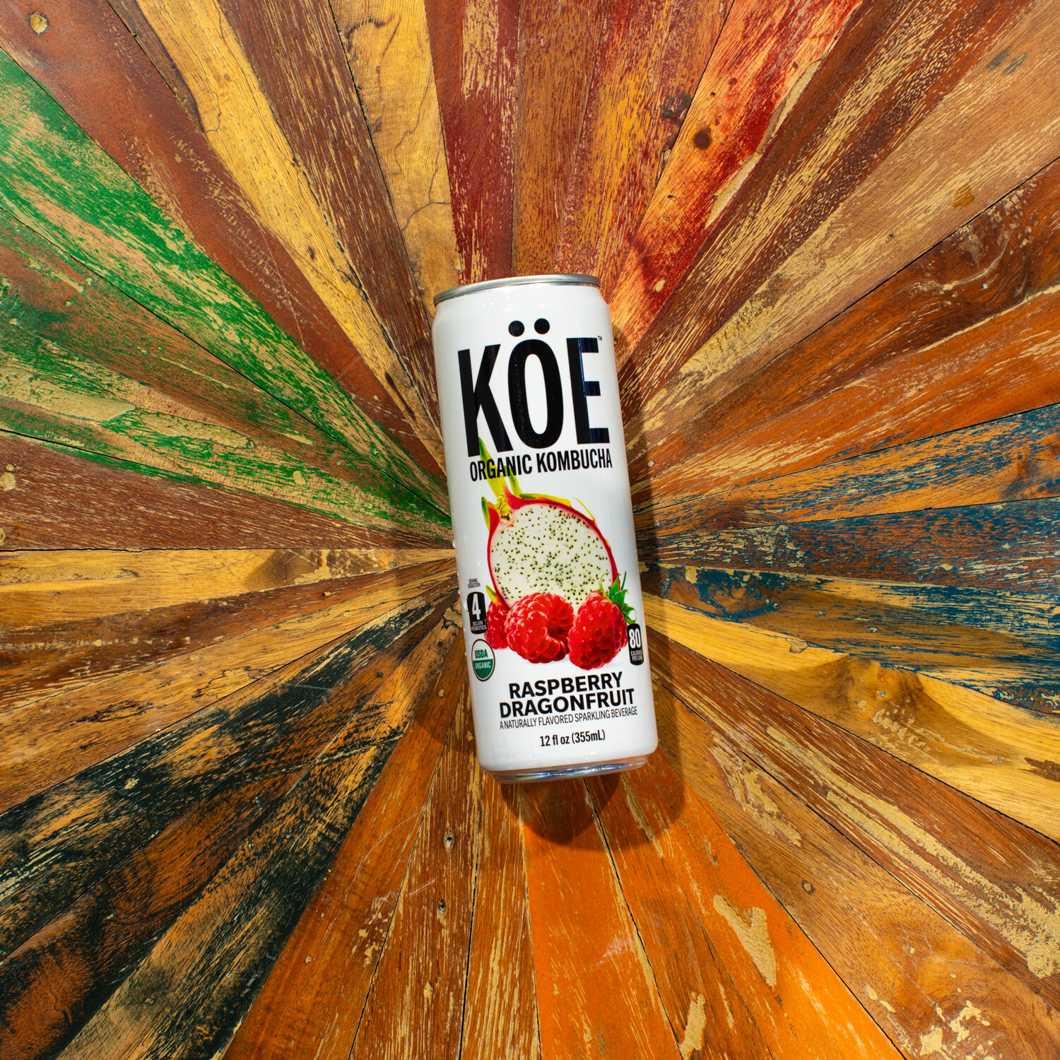 A single Koe kombucha can on a radial pattern of weathered painted boards.