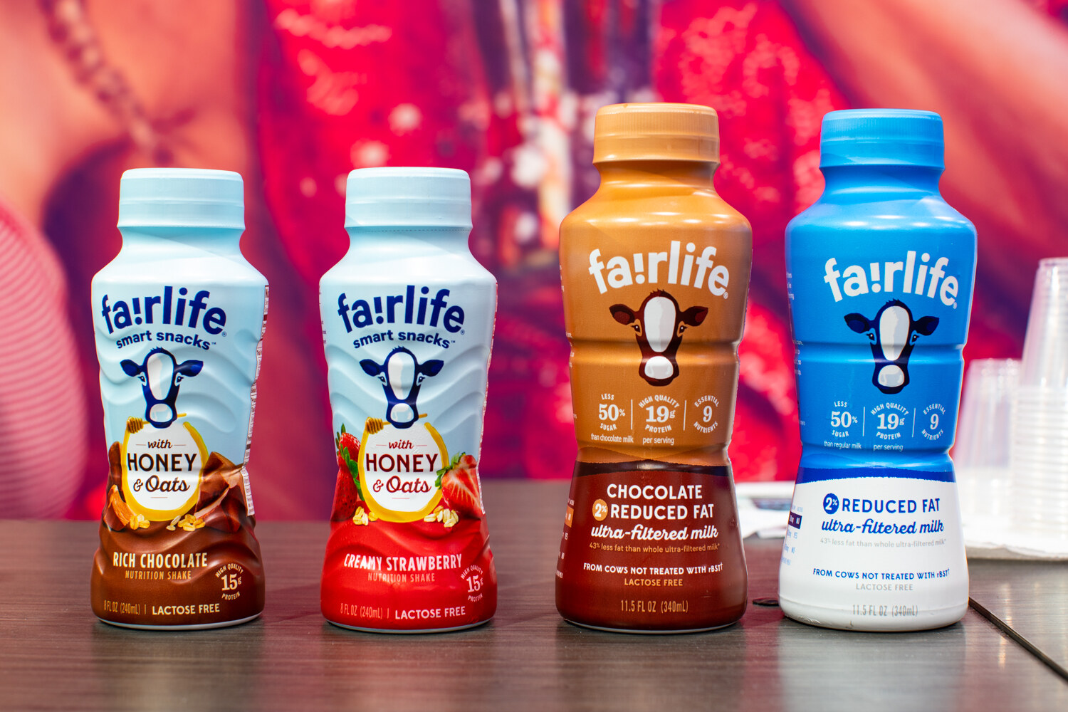 Four fairlife bottles in blue, red and brown on a counter against a bright backdrop.