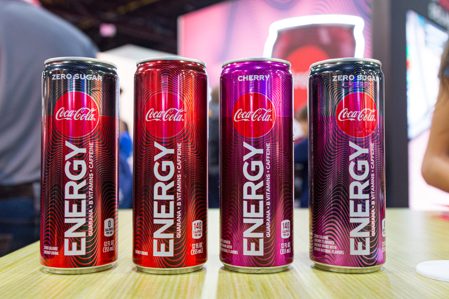 Red and purple Coca-Cola Energy cans in a row in front of a lit red backdrop.