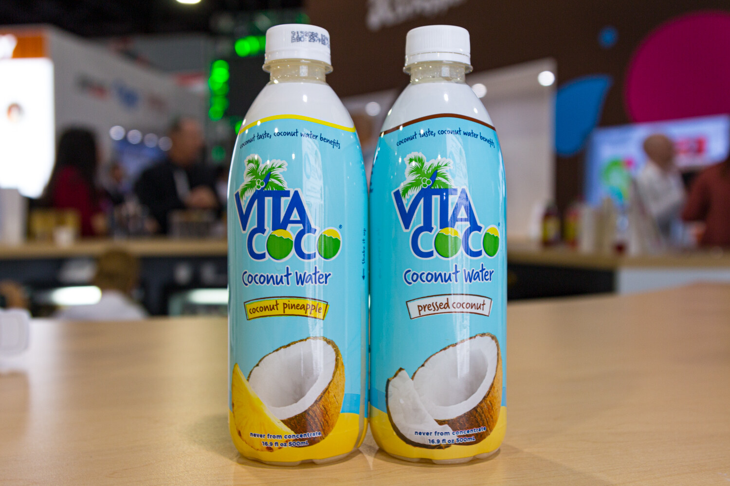 Two bottles labeled Vita Coco Coconut Water with a blurred expo hall behind them.