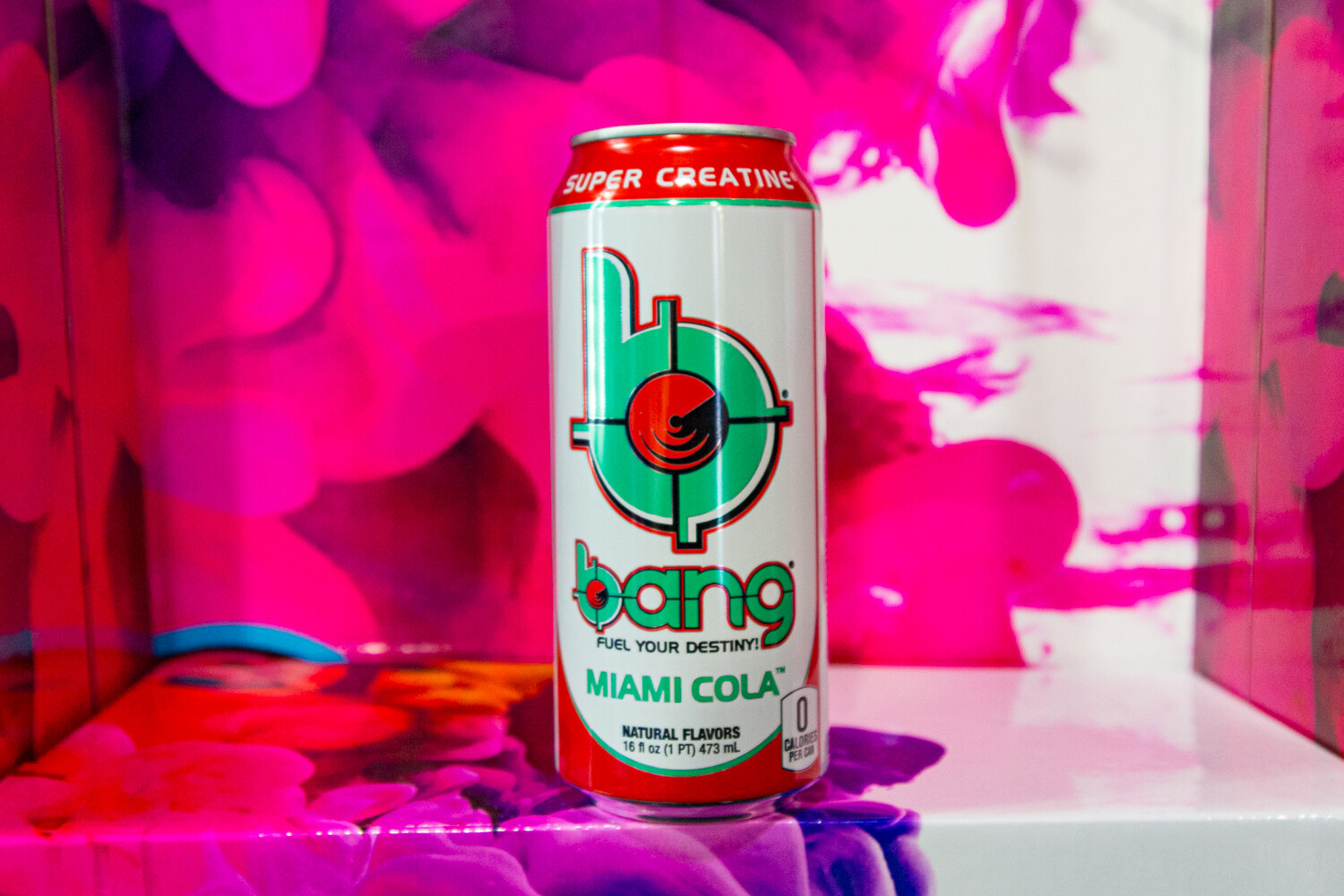 A white and teal Bang Energy Miami Cola can in front of swirling magenta paint.