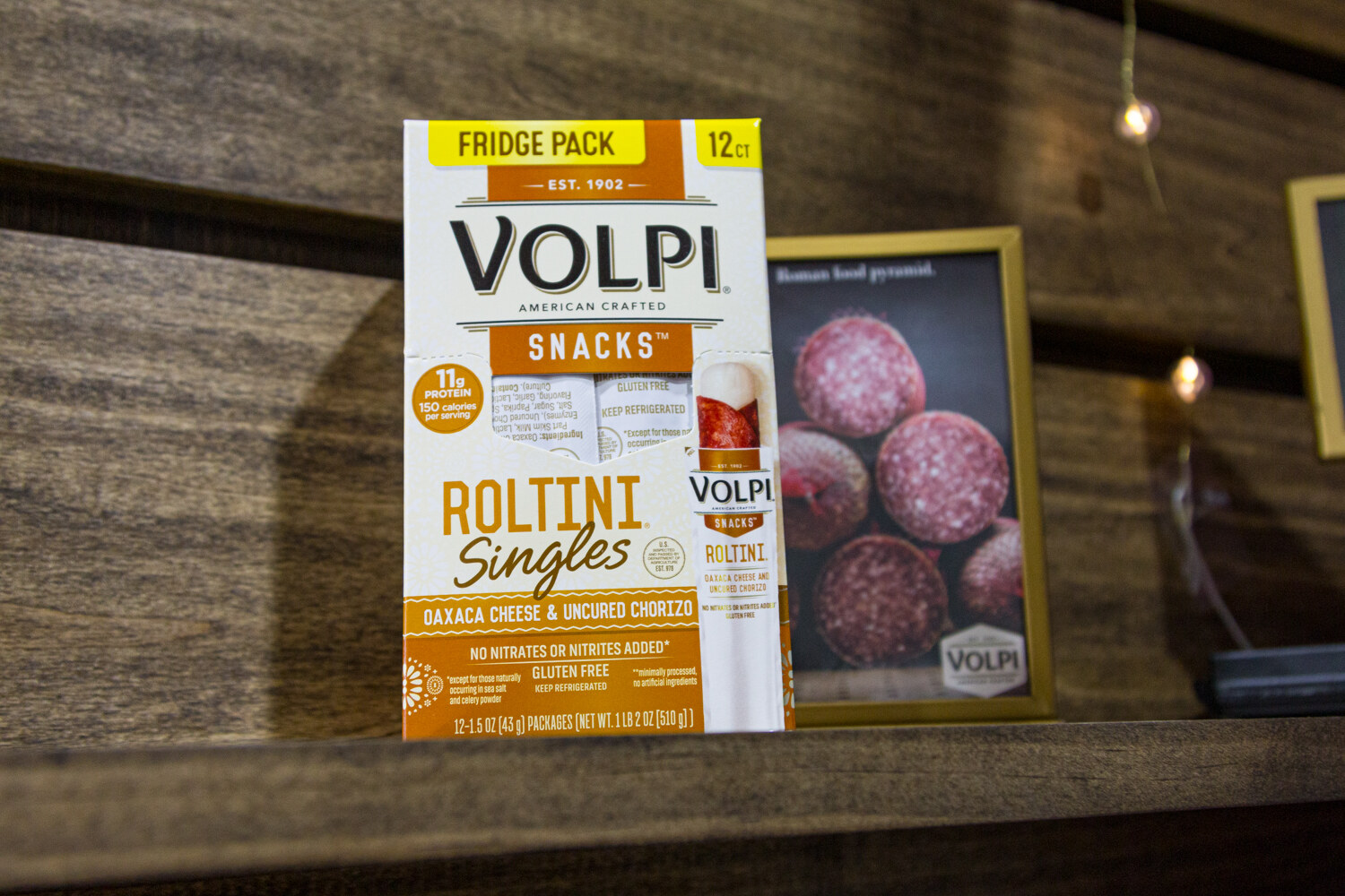 A Volpi Snacks Roltini Singles box with Oaxaca cheese and uncured chorizo on a dark wood shelf.