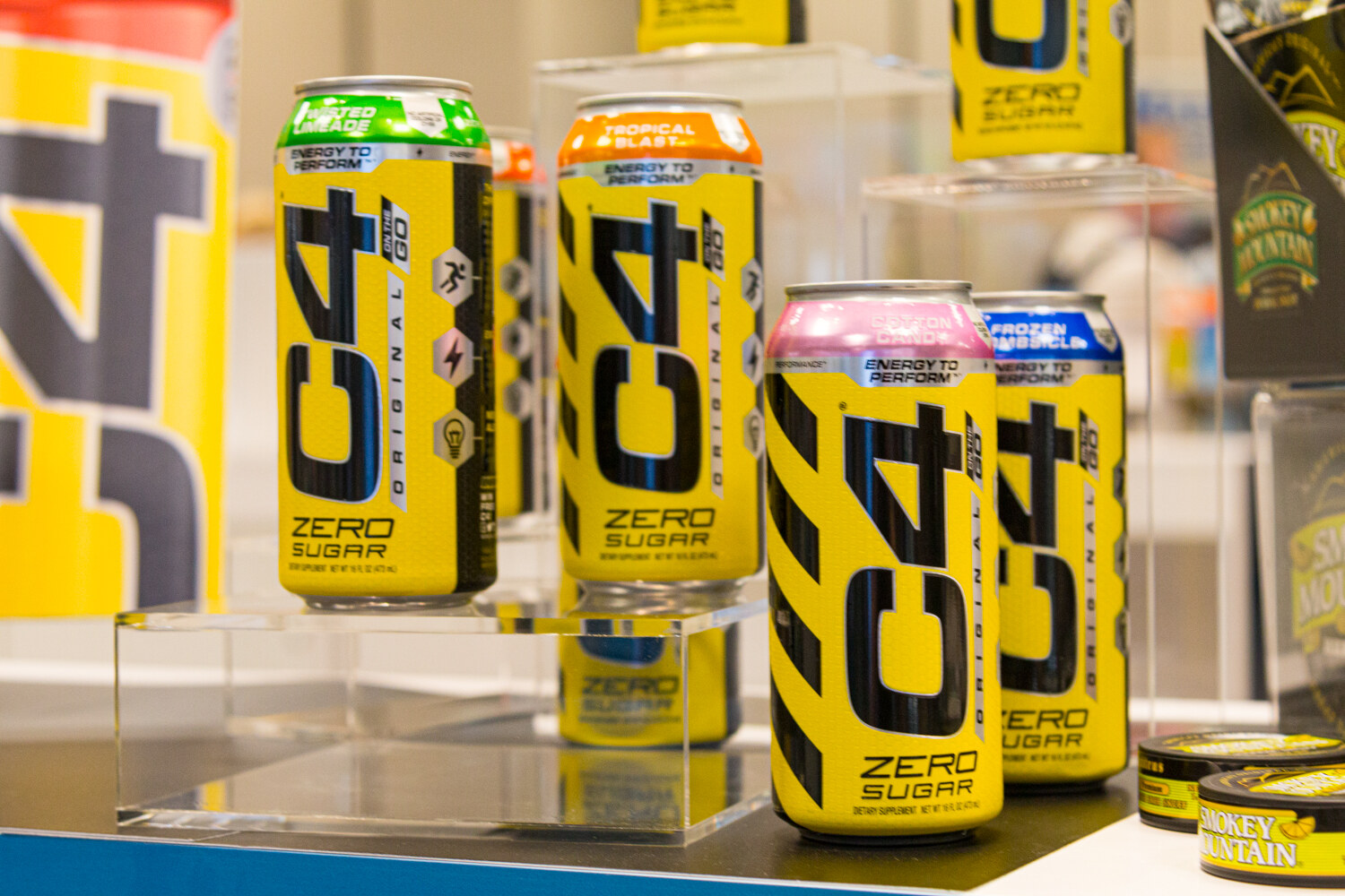 Yellow C4 Zero Sugar cans stacked on clear risers in front of a C4 display.