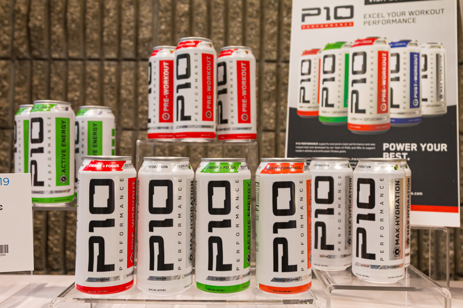 Red, white, green and gray P10 cans on a shelf with a P10 workout poster behind.