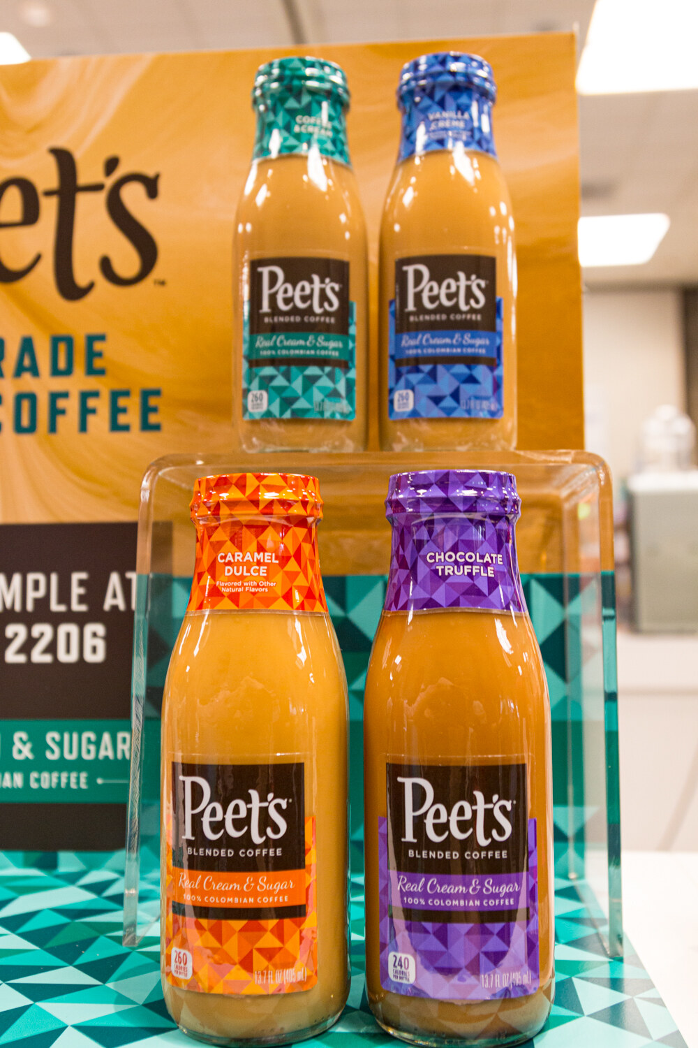 Four Peet's Coffee bottles in teal, blue, orange and purple on a lit stand.