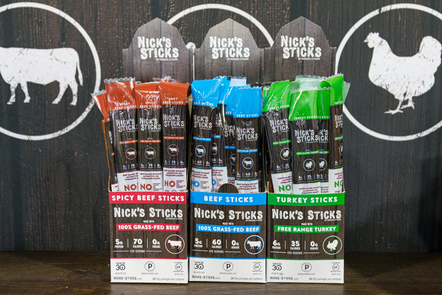 Three Nick's Sticks display boxes in orange, blue and green in front of a dark wall with a cow and a chicken logo.
