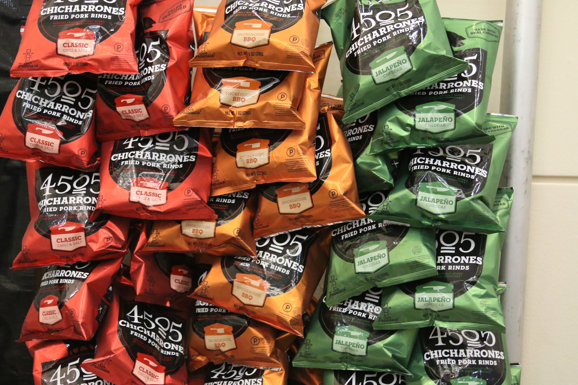 Piles of red, orange and green 4505 Chicharrones fried pork rinds bags.