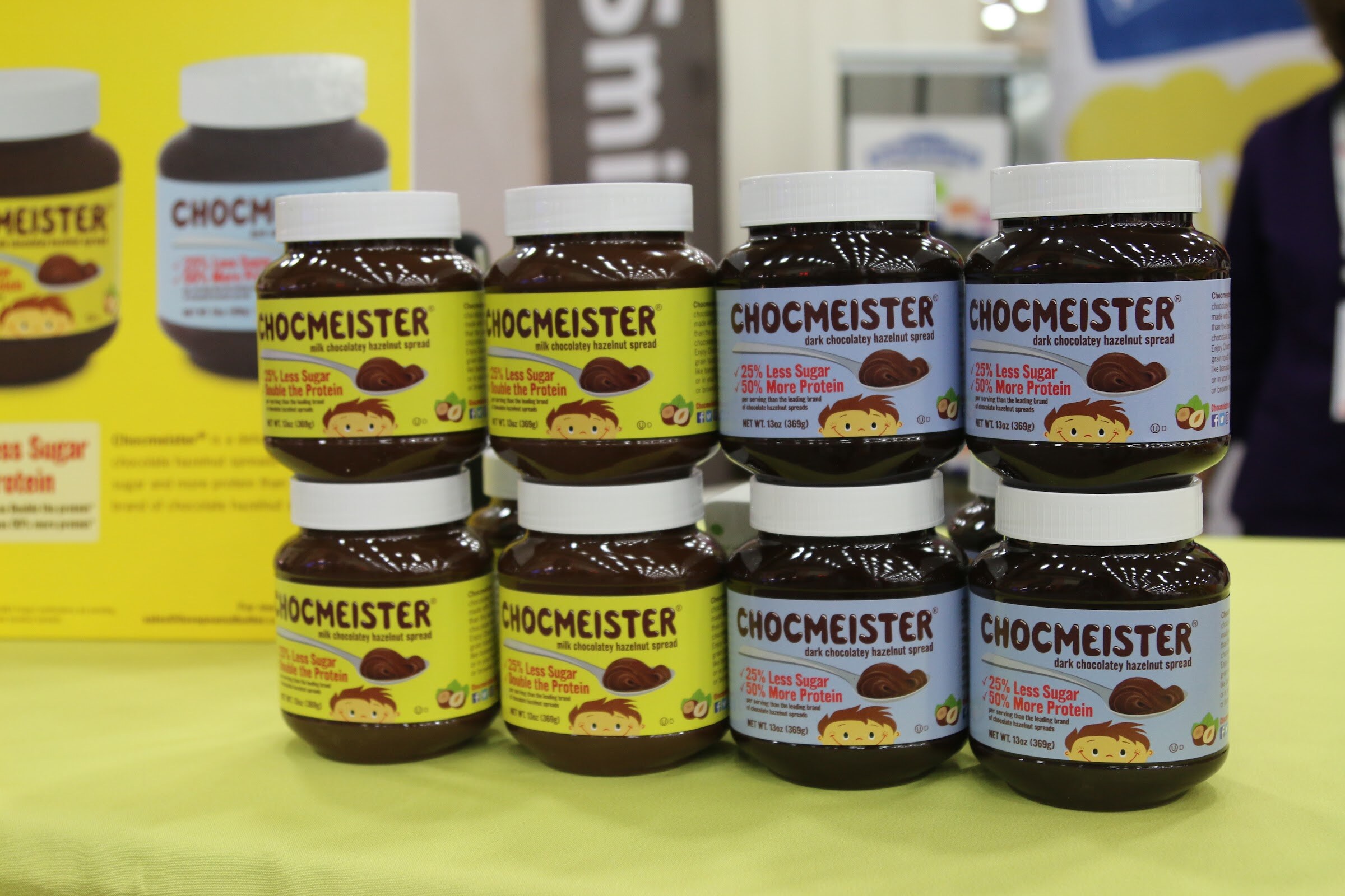 Eight jars of Chocmeister spread in milk and dark chocolate varieties stacked two high on a lime tablecloth.