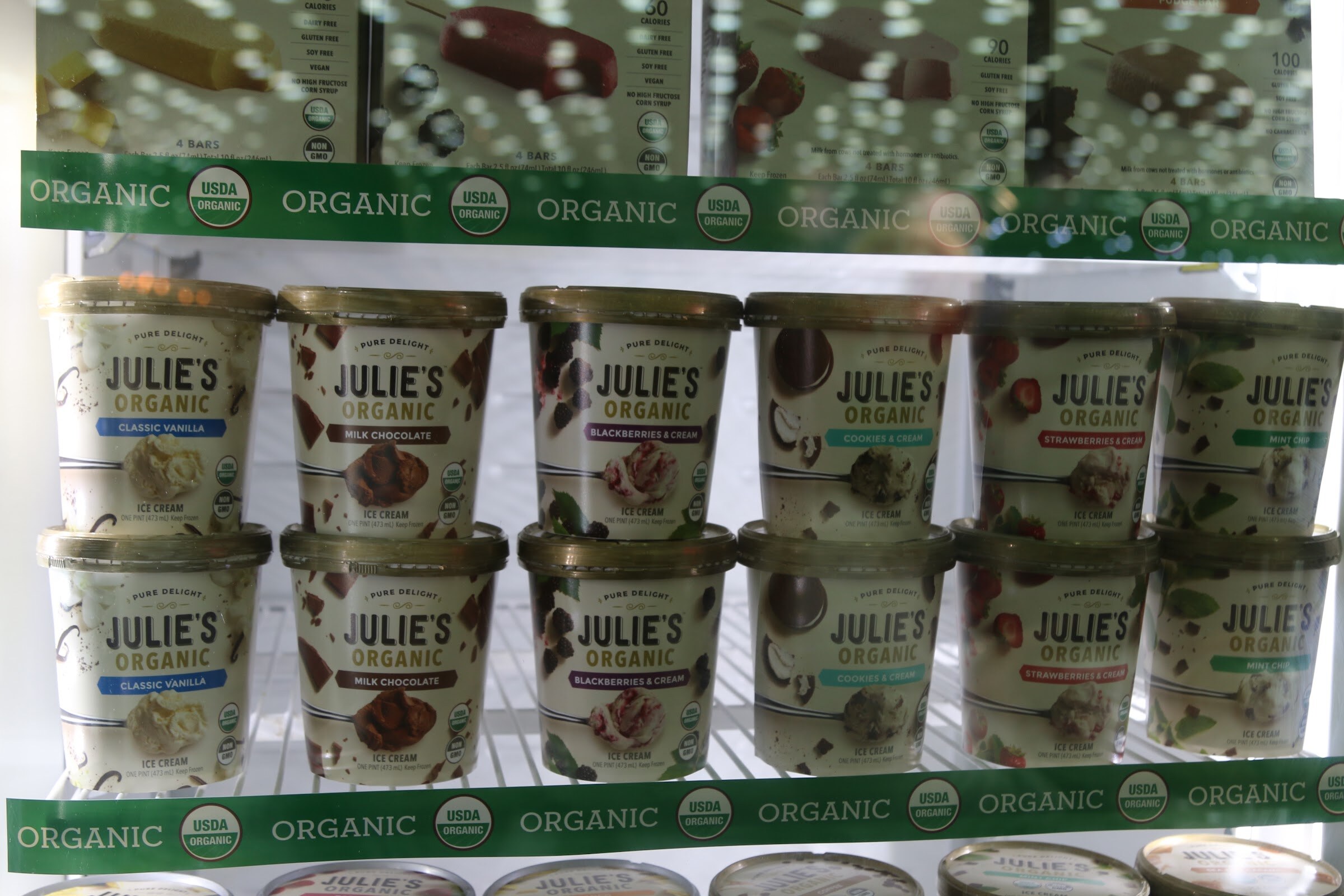 Rows of Julie's Organic ice cream tubs in flavors including classic vanilla, milk chocolate and strawberries and cream in an open freezer.