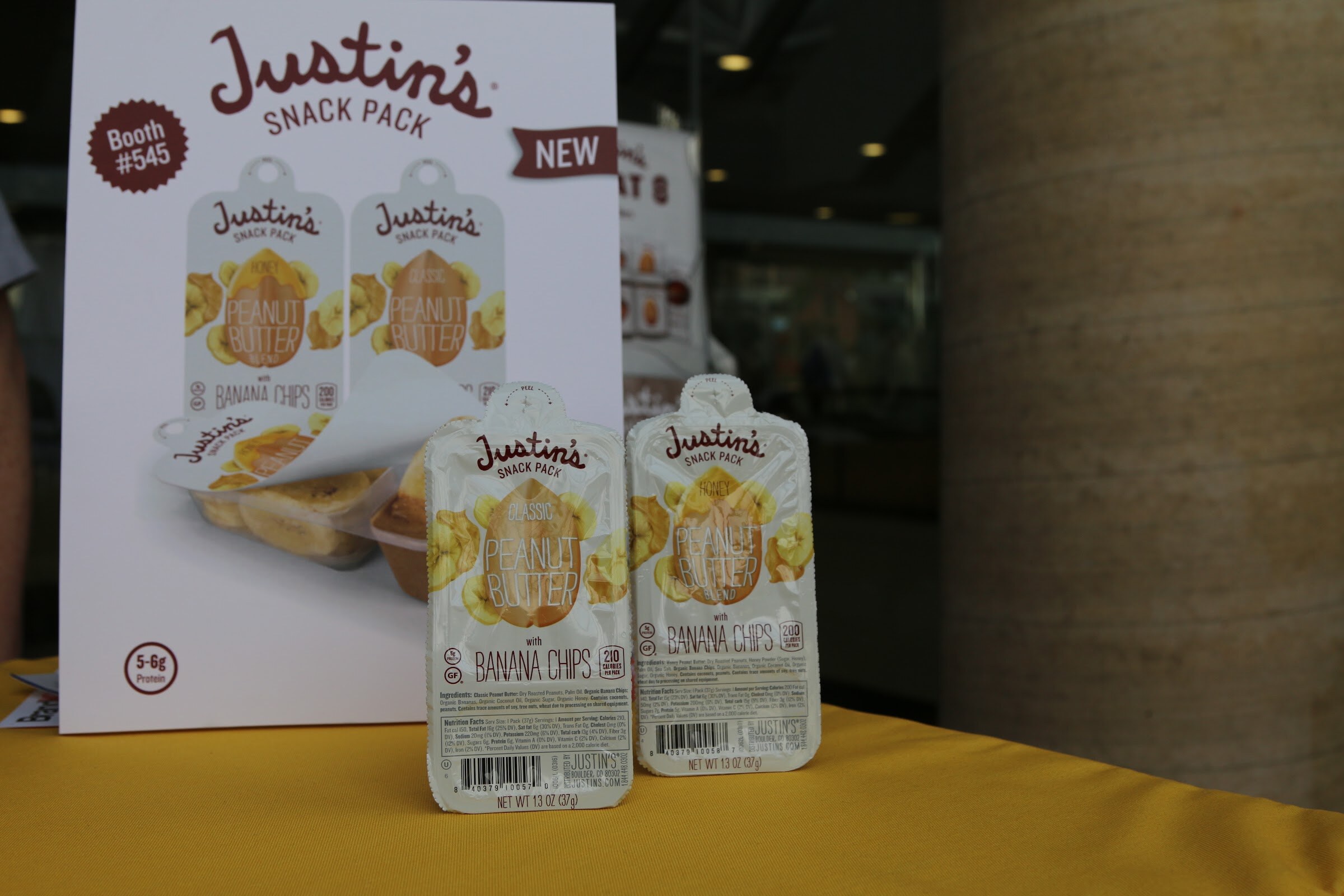 A Justin's Snack Pack booth sign reading Booth 545 with two peanut butter with banana chips pouches in front of it.