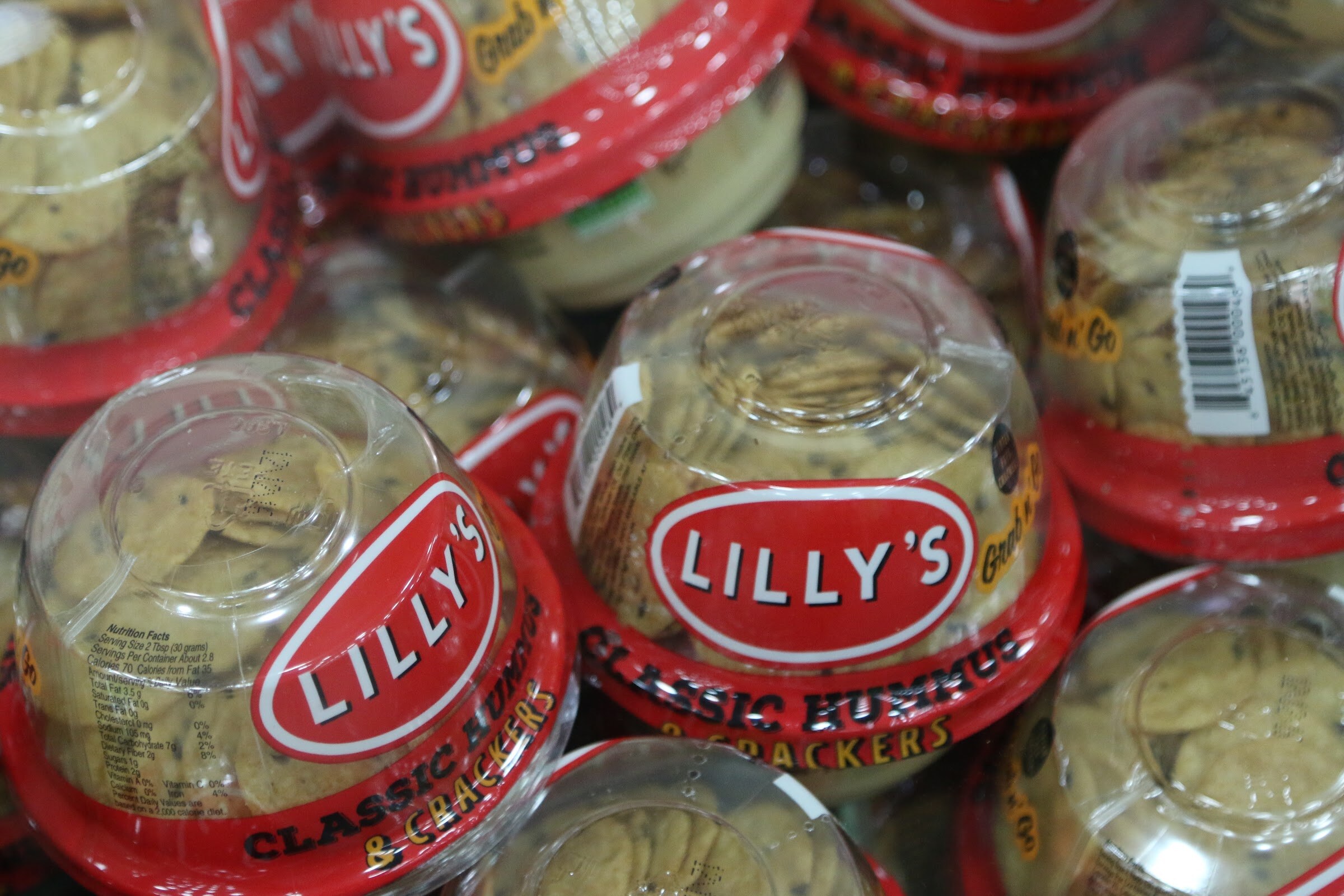 Clear domed Lilly's hummus and cracker cups with red lids stacked together in a cooler.