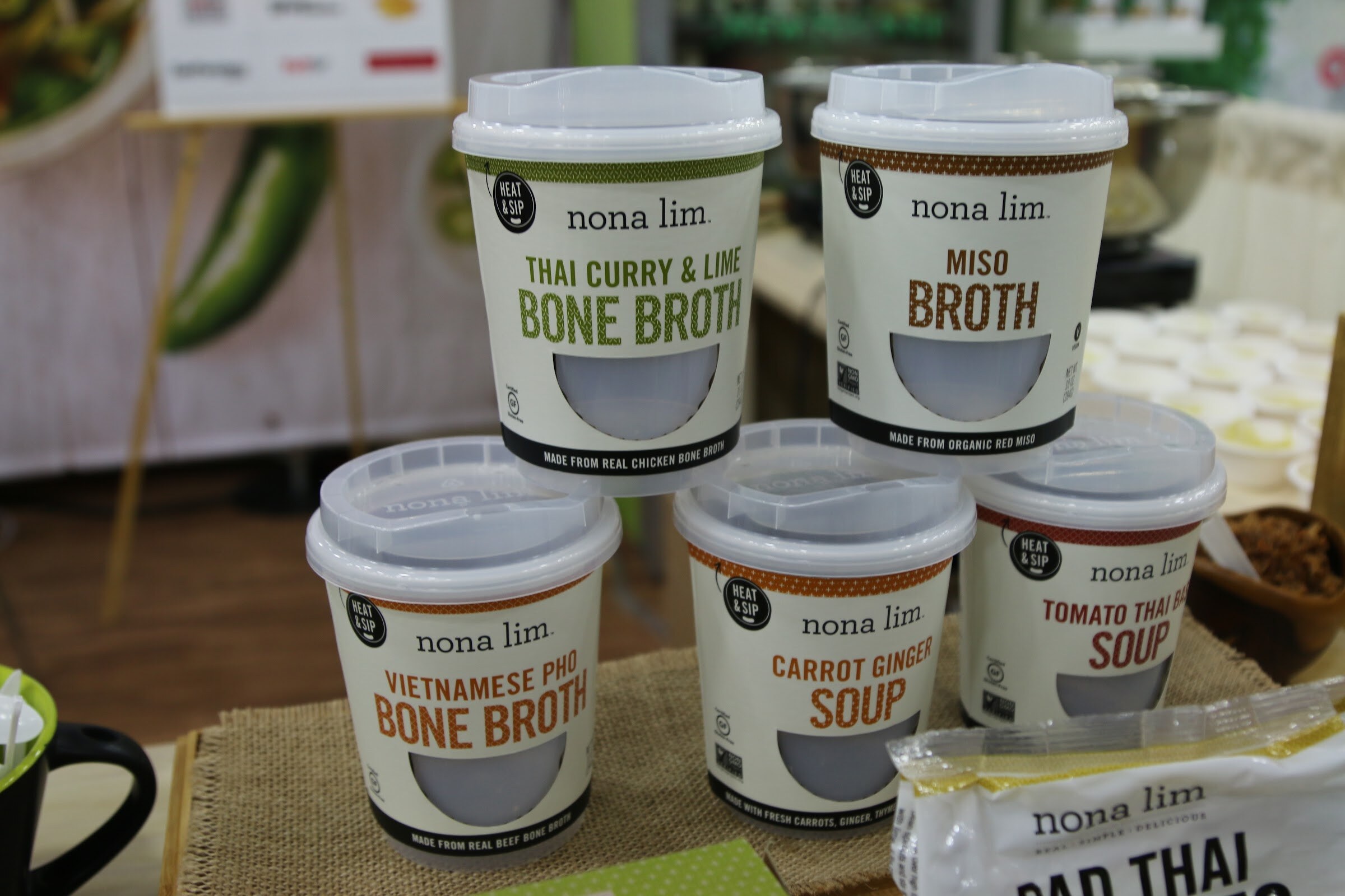Five white Nona Lim cups stacked in a pyramid on a burlap runner with a Nona Lim pouch at the lower right.
