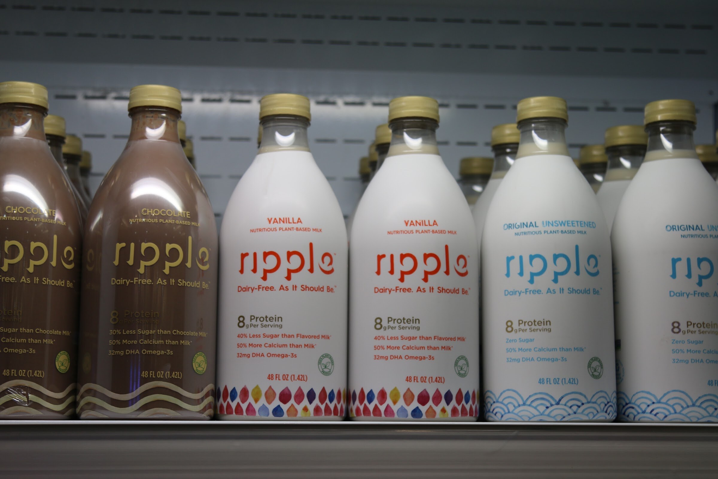 Rows of Ripple bottles with gold caps and colorful droplet patterns on a chilled shelf.