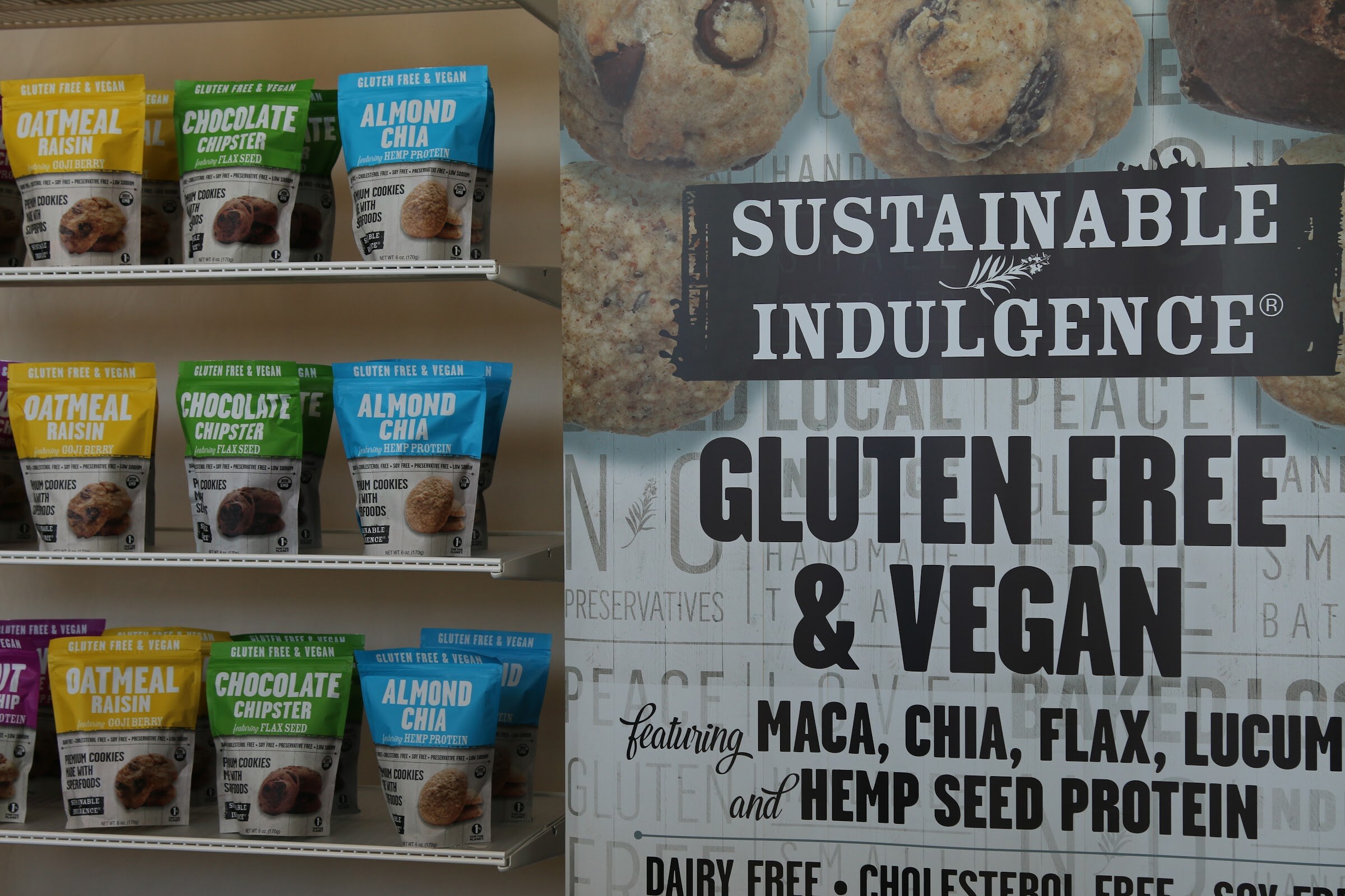 Shelves of colorful Sustainable Indulgence cookie bags next to a large sign reading Gluten Free and Vegan.