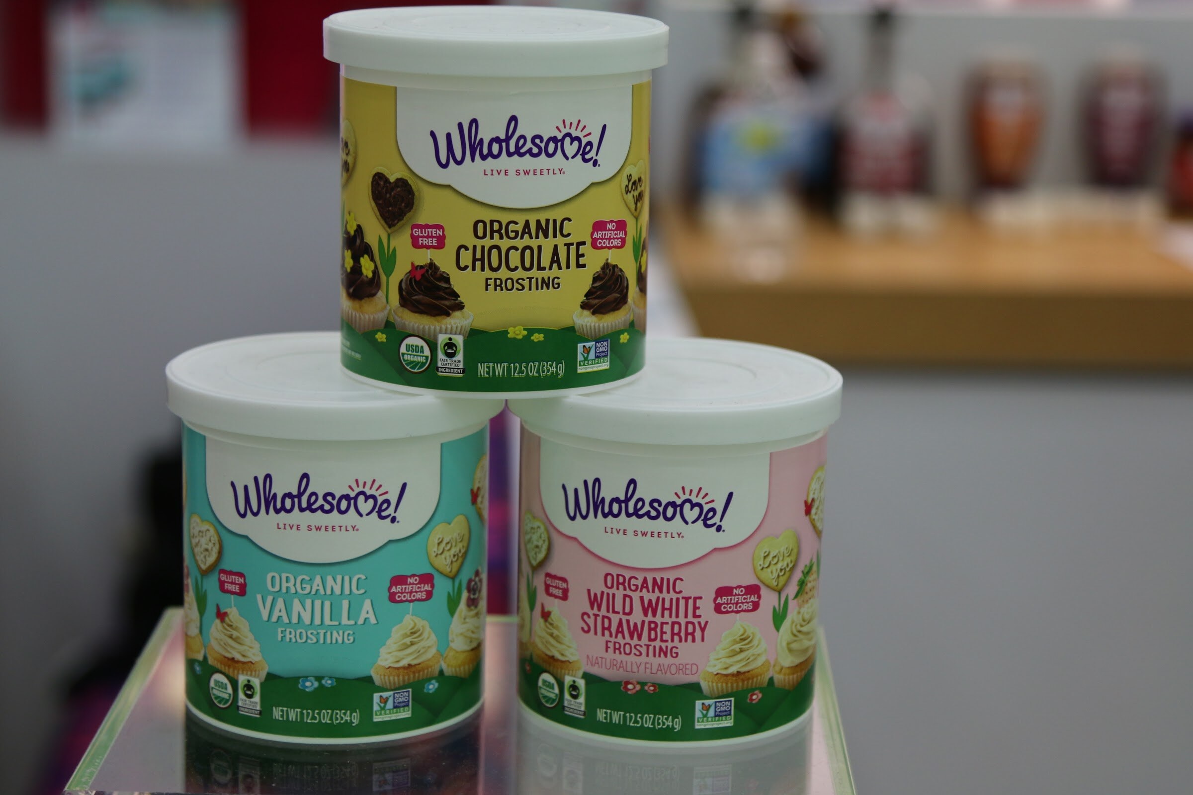 Three Wholesome frosting canisters stacked in a pyramid on a glass shelf.