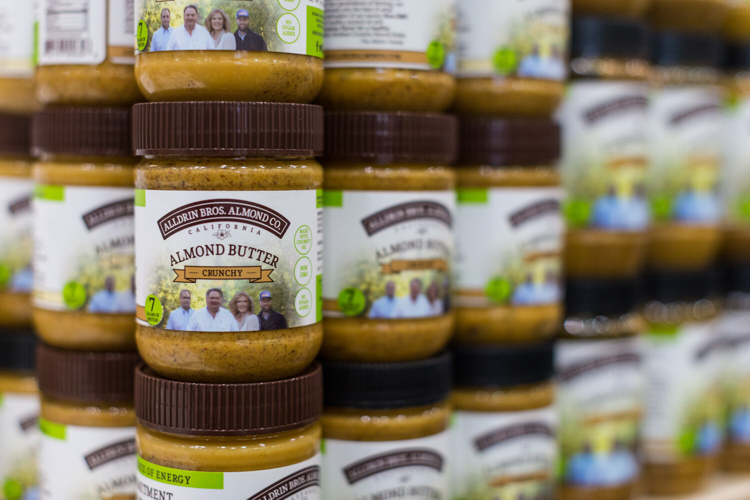 Stacked jars of Alldrin Bros. Almond Co. almond butter, one in sharp focus and the rest fading into blur.