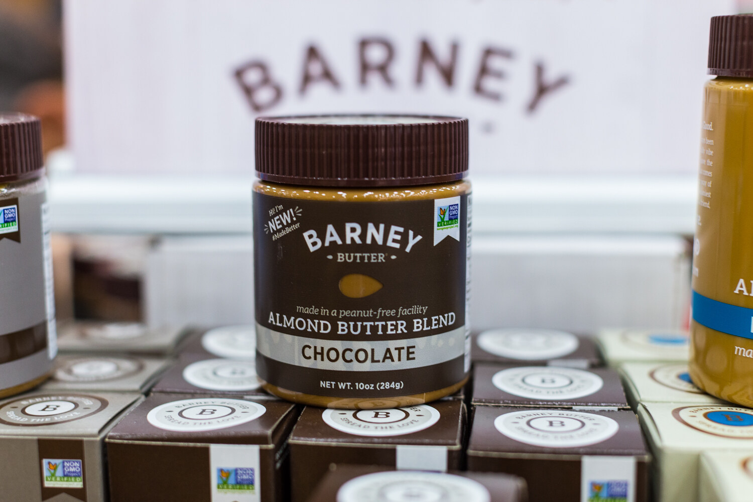 A single jar of Barney Butter Almond Butter Blend Chocolate on top of boxes, with a Barney sign blurred behind.