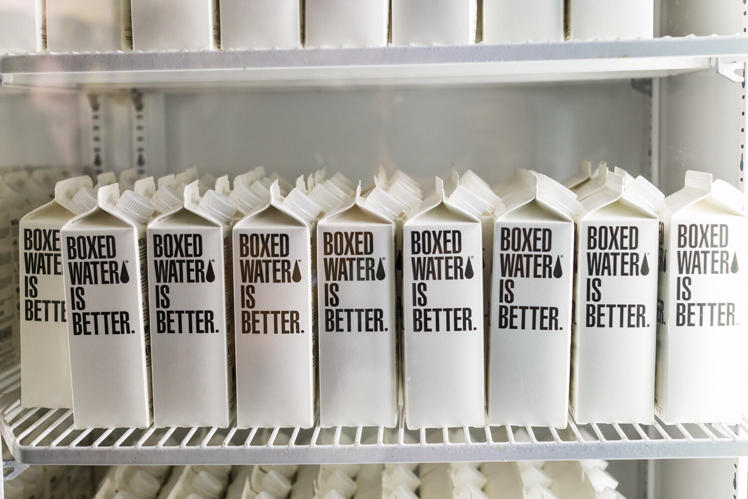 White Boxed Water Is Better cartons lined up on wire cooler shelves.