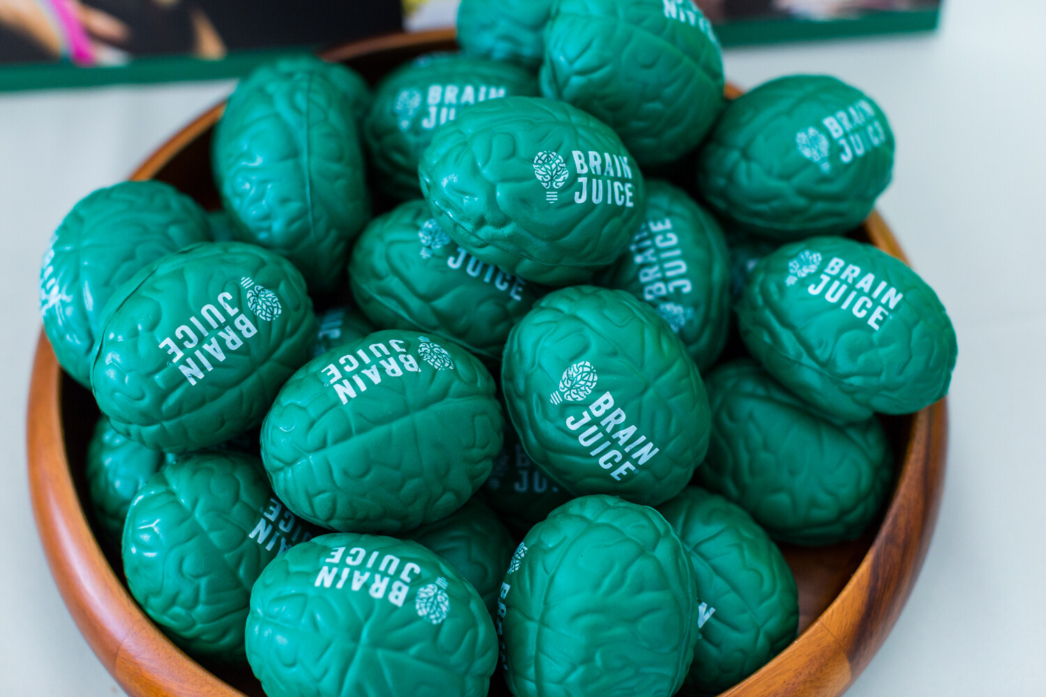 A wooden bowl heaped with green foam brain-shaped stress toys printed Brain Juice.
