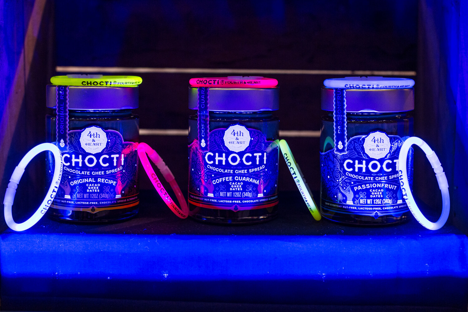 Three Chocti jars in dark blue light with neon yellow, pink and white glow bracelets on and around them.