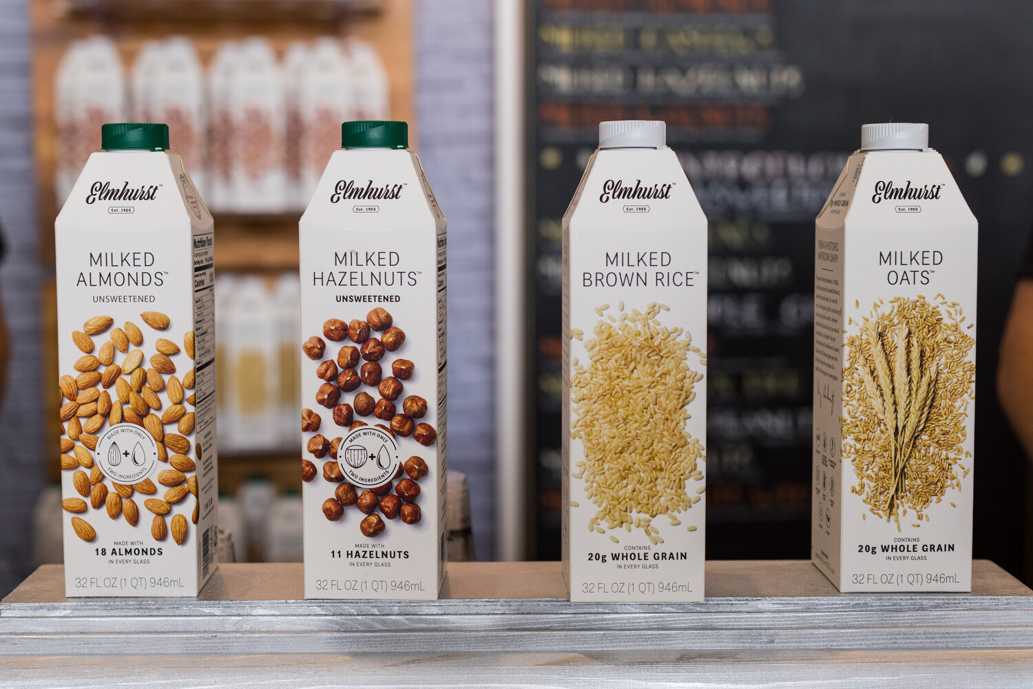 Four white Elmhurst cartons of Milked Almonds, Hazelnuts, Brown Rice and Oats, each printed with its main ingredient.